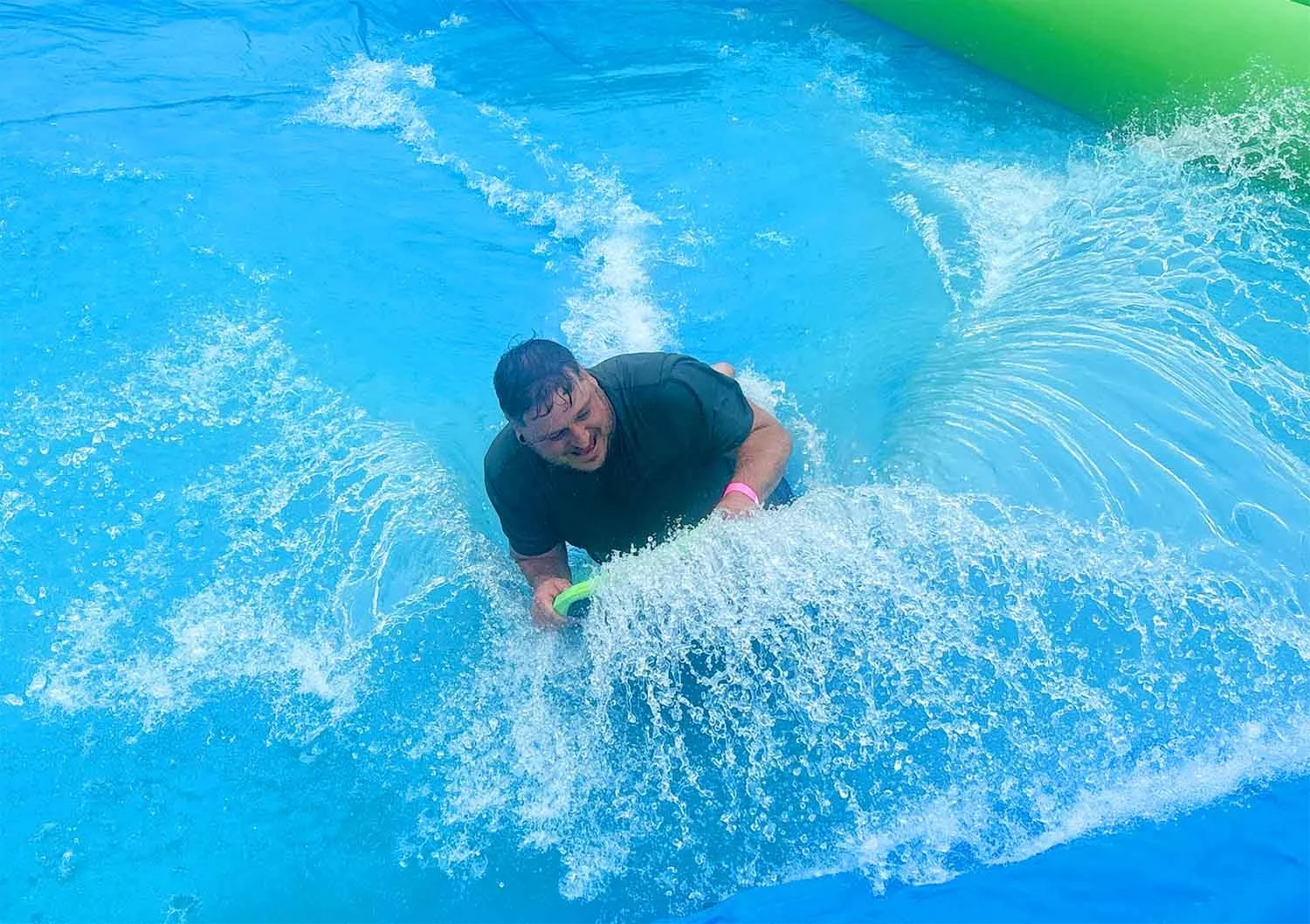 A man riding a bodyboard on the giant slip and slide in Cornwall, holding onto the edge with a joyful expression.