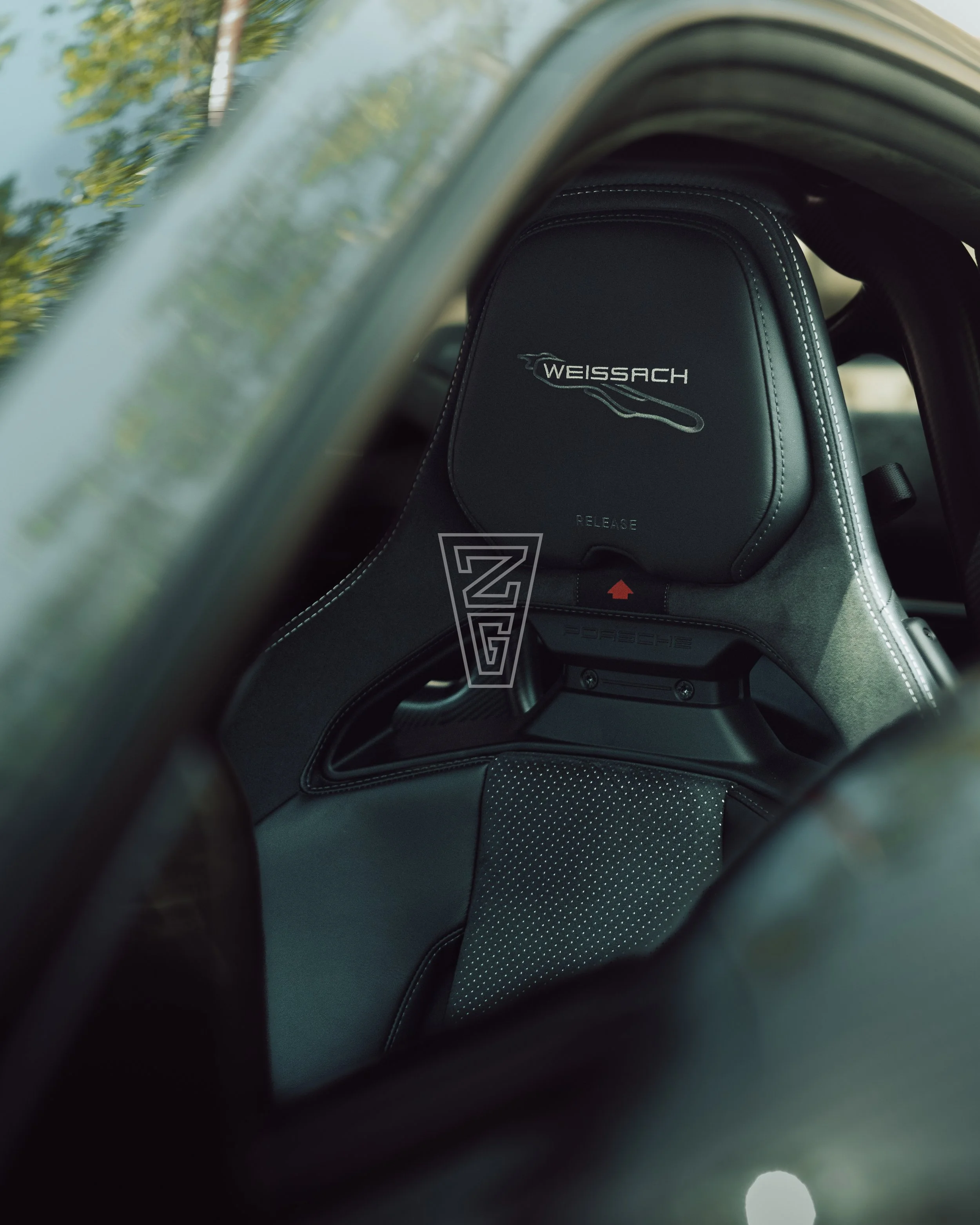 Close-up view of a black car seat inside a vehicle, with the brand name 'WEISSACH' and a logo embroidered on the headrest. The interior stitching is visible, and part of the rear window and dashboard can be seen in the background.