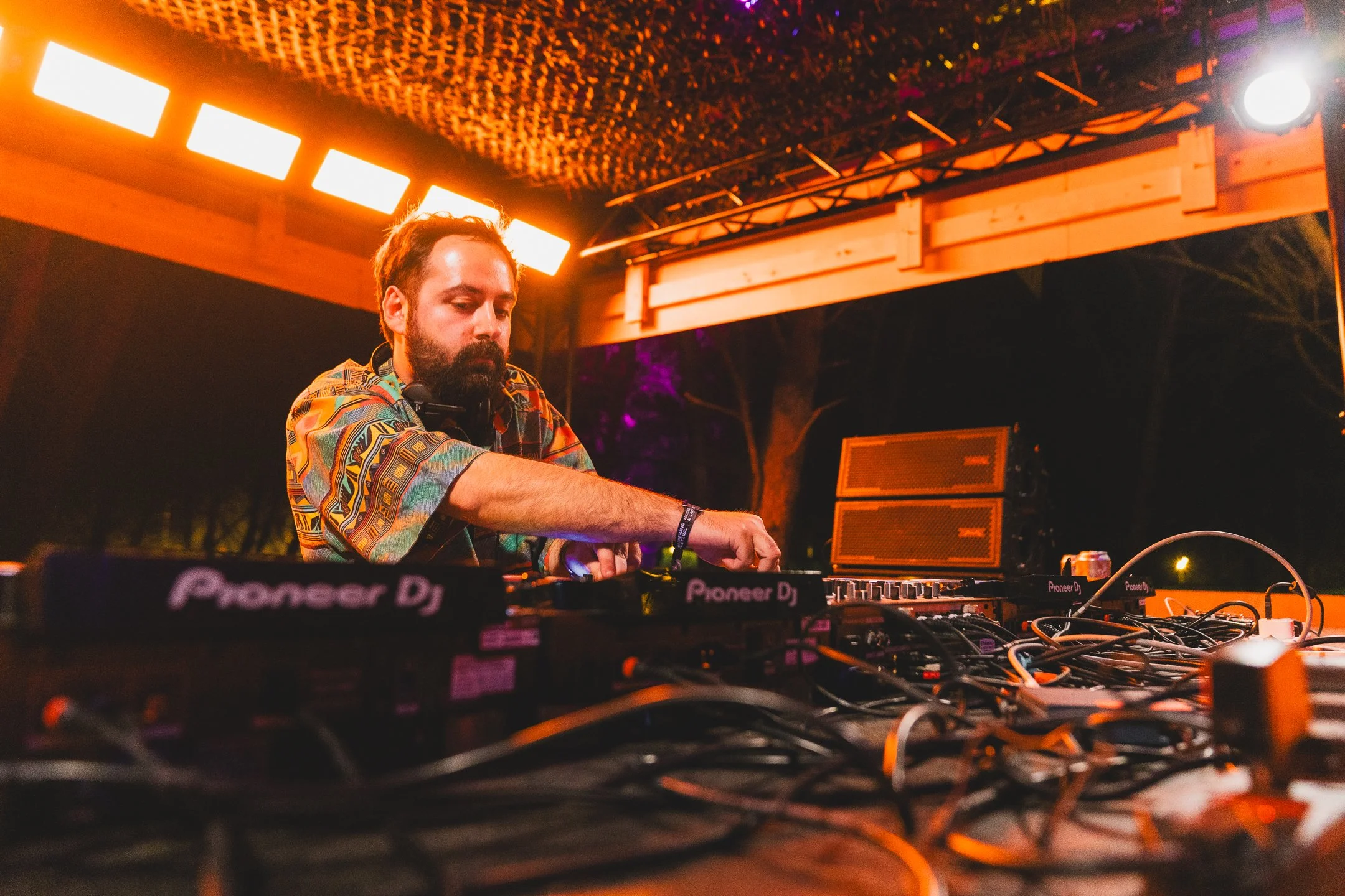 DJ in a colorful shirt mixing music on professional Pioneer decks under warm stage lights.