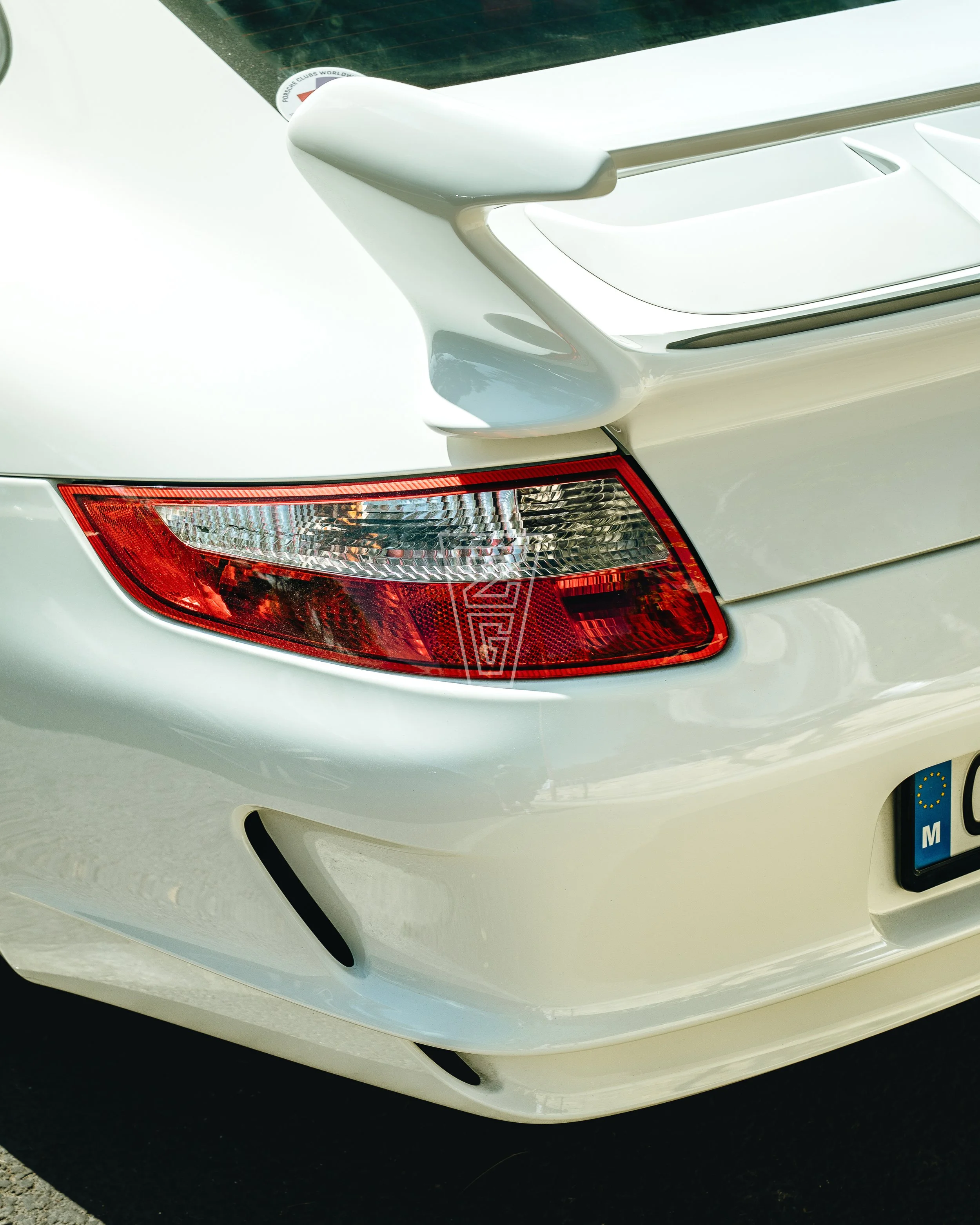 Close-up of the rear end of a white car, highlighting the tail light, rear bumper, and rear wing.
