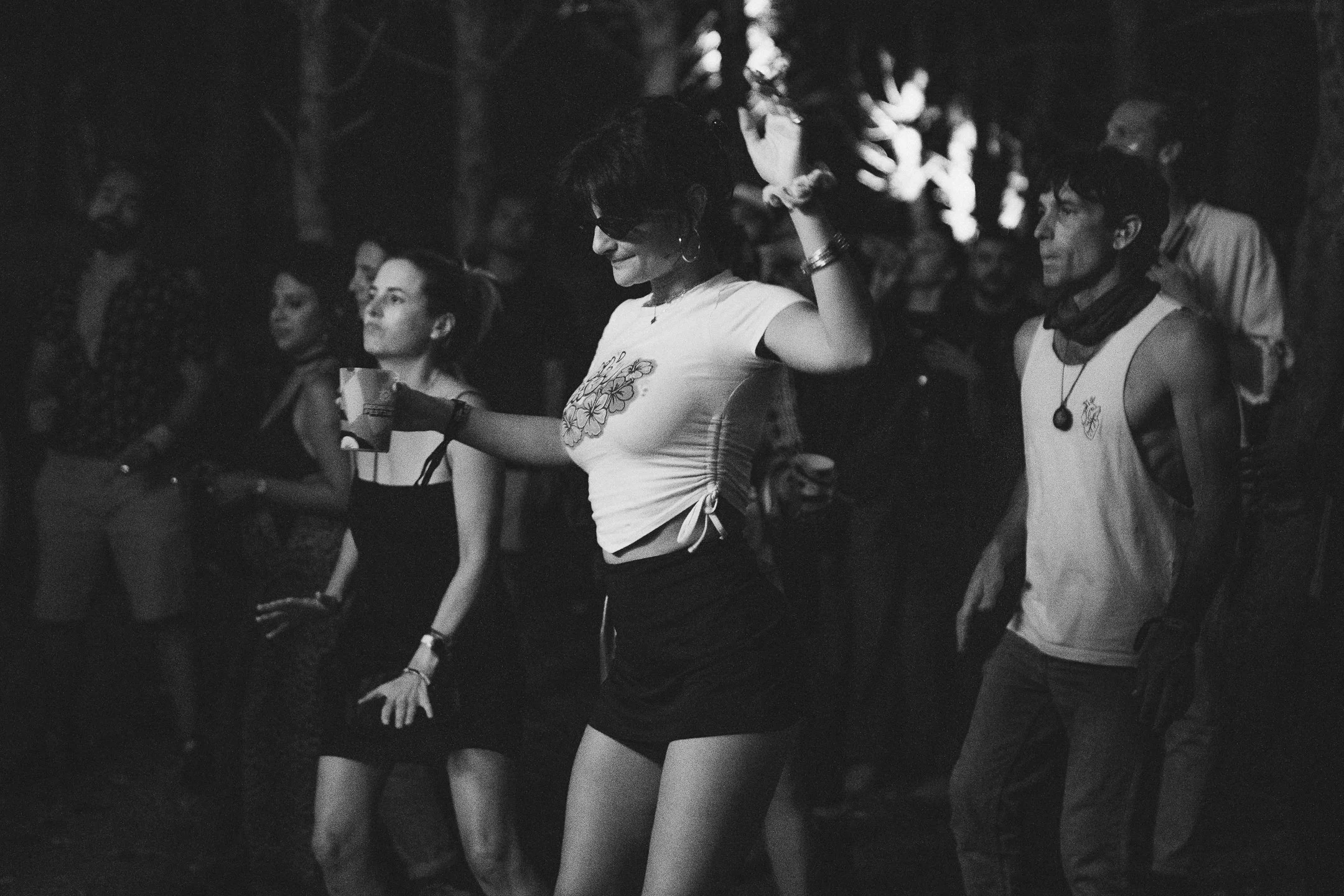 People dancing at a night event in black and white with a woman in a floral top in focus.