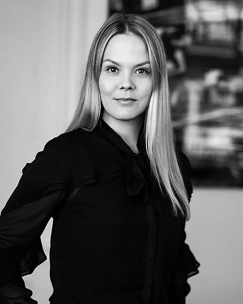 Porträtt av en kvinna med långt blont hår, svart blus, i svartvitt.