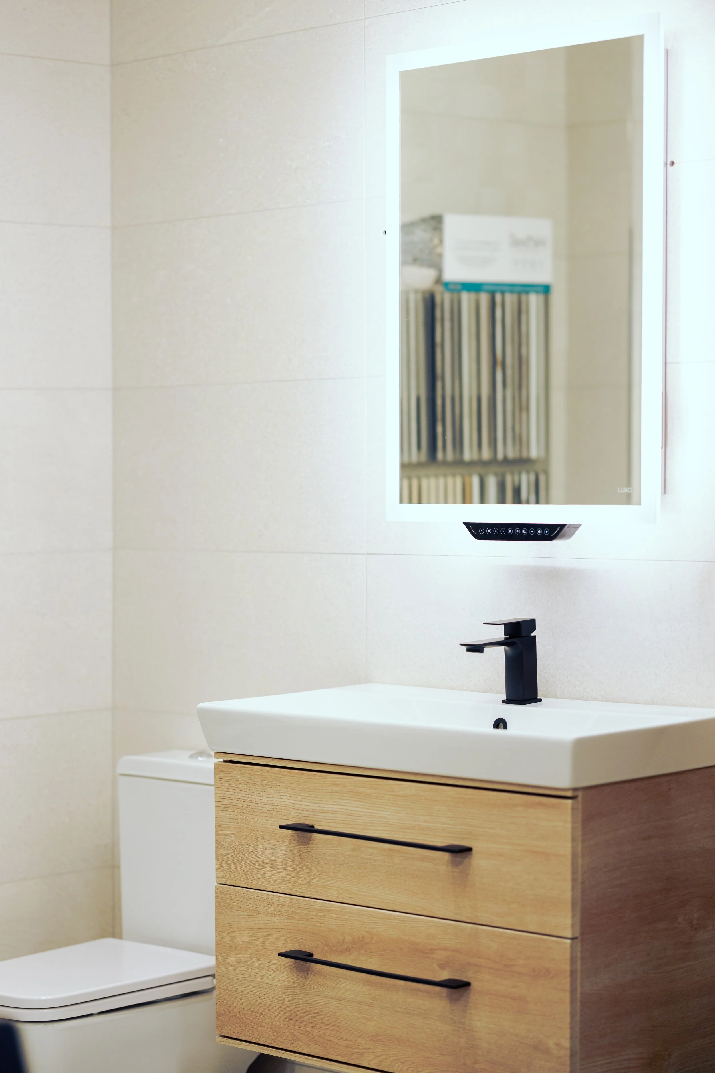 A modern bathroom with dark blue tiled wall, a white pedestal sink, a white toilet, and a round mirror with a decorative frame.