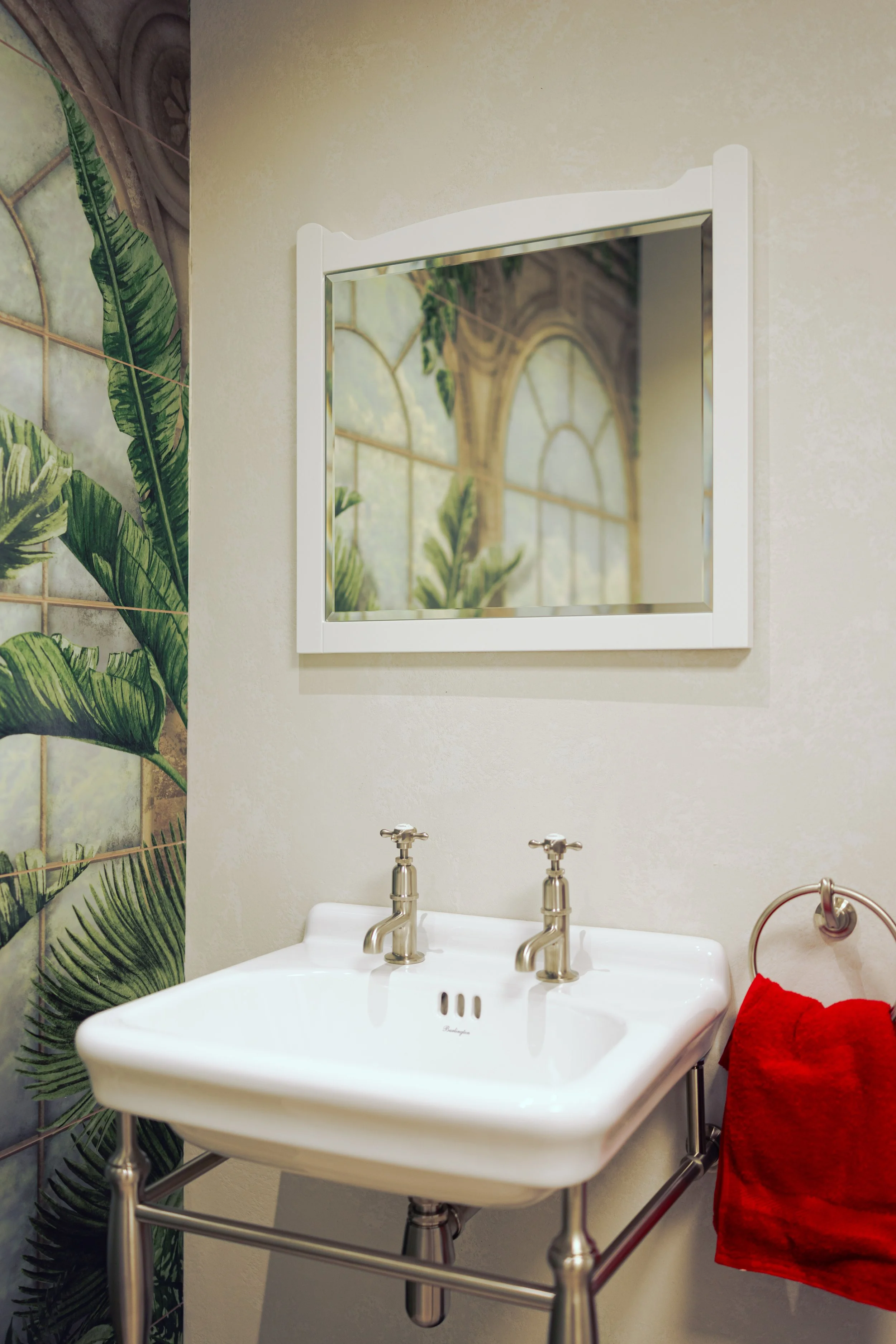 A modern bathroom with a white toilet and a green cabinet, decorated with small potted plants on a white countertop. The walls are tiled with floral and neutral-colored tiles.