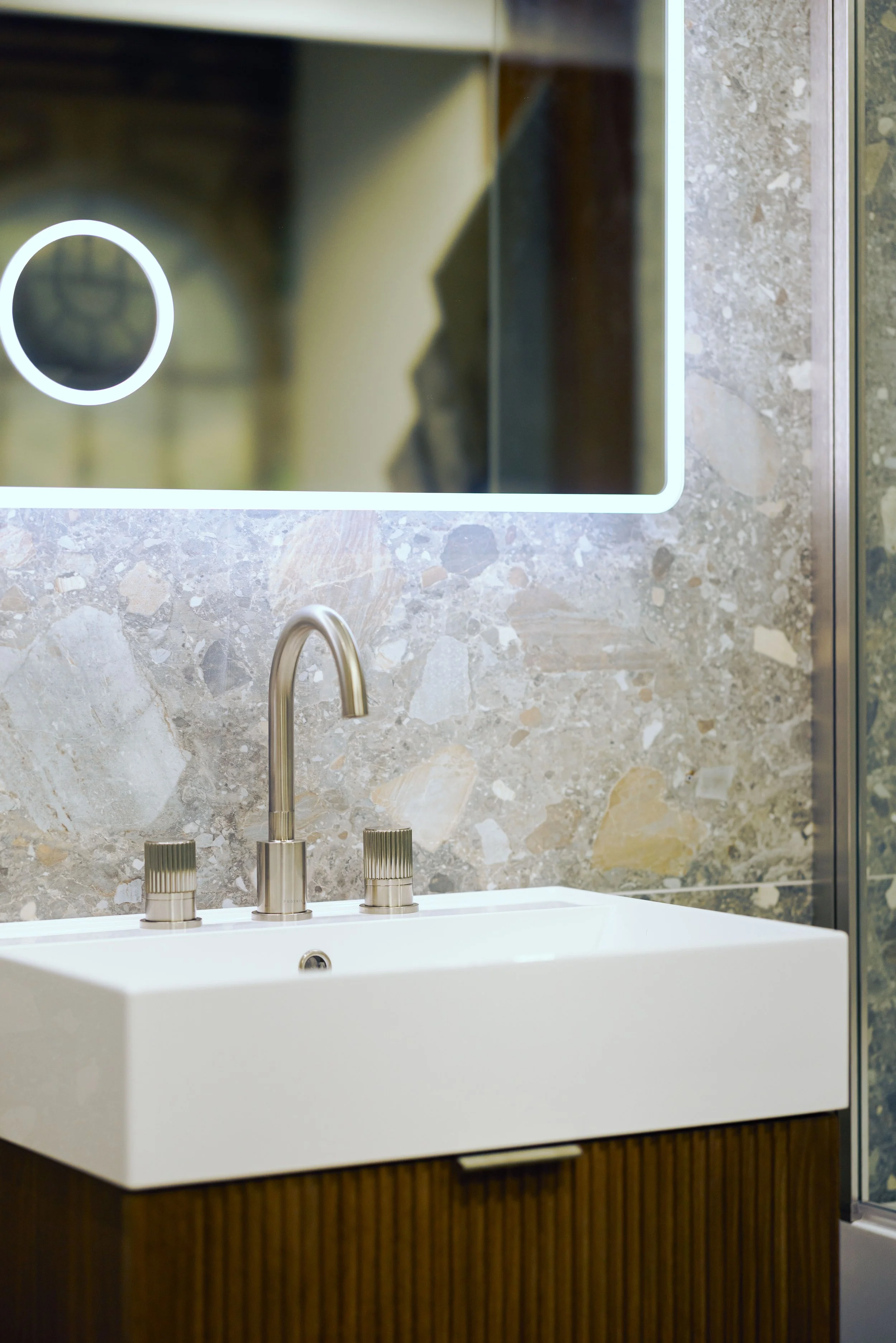 Modern bathroom vanity with gray cabinetry and a white countertop, set against a dark textured wall with a large, curved mirror reflecting ceiling lights.