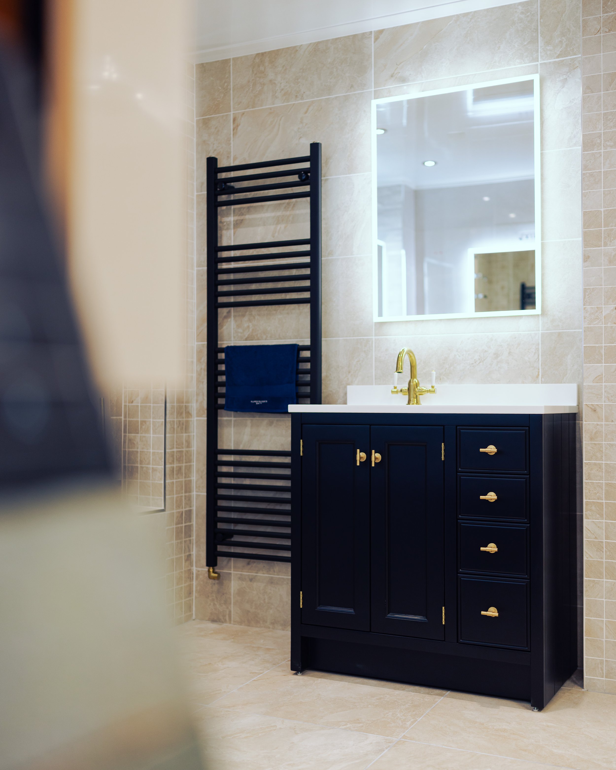 Modern bathroom with marble walls and floor, a white and black vanity with gold accents, a round mirror, and a gold towel rack.