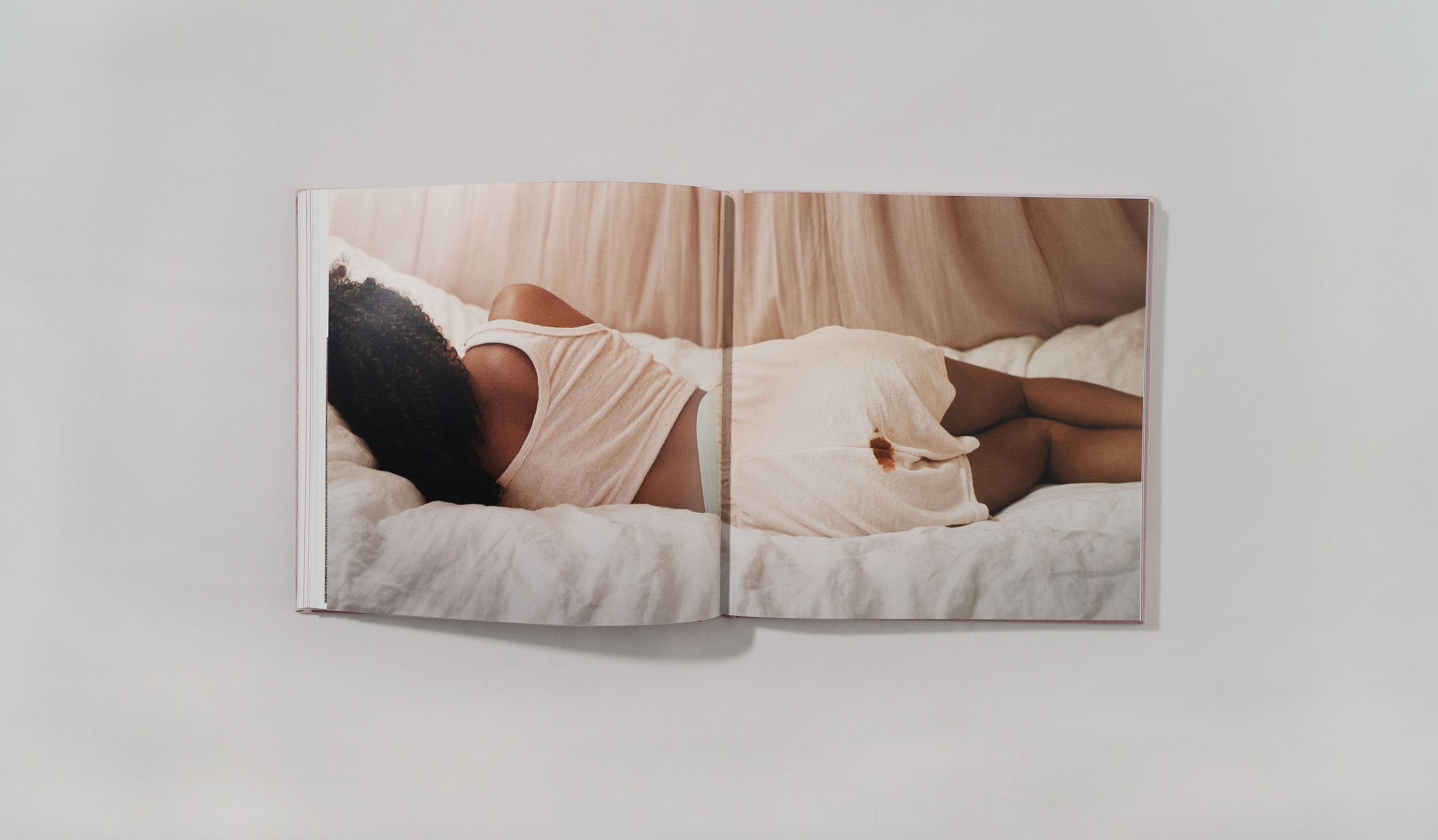 Open book with photo of a person sleeping on a bed, lying on her side, with dark curly hair, wearing a light pink top and matching shorts, on white bed with wooden headboard.
