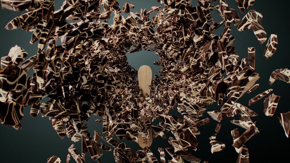 A wooden spatula surrounded by a swirling vortex of torn chocolate bar pieces with white and dark chocolate swirl patterns.