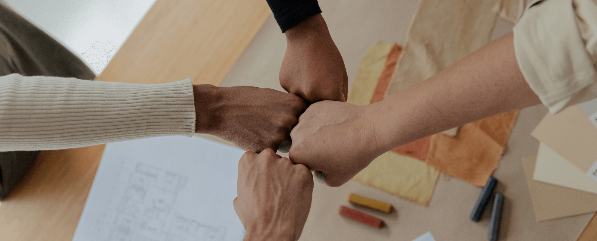Quatre personnes de différentes origines rejoignent leurs poings en symbole de solidarité sur un bureau.