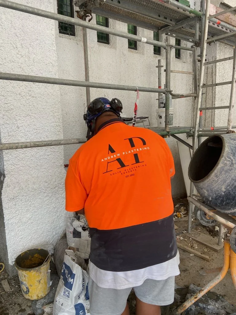 Andrew Plastering team member repairing exterior wall on construction site.