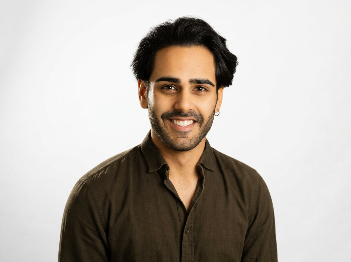 A smiling man with black hair, facial hair, and a small earring, wearing a dark brown shirt against a white background.