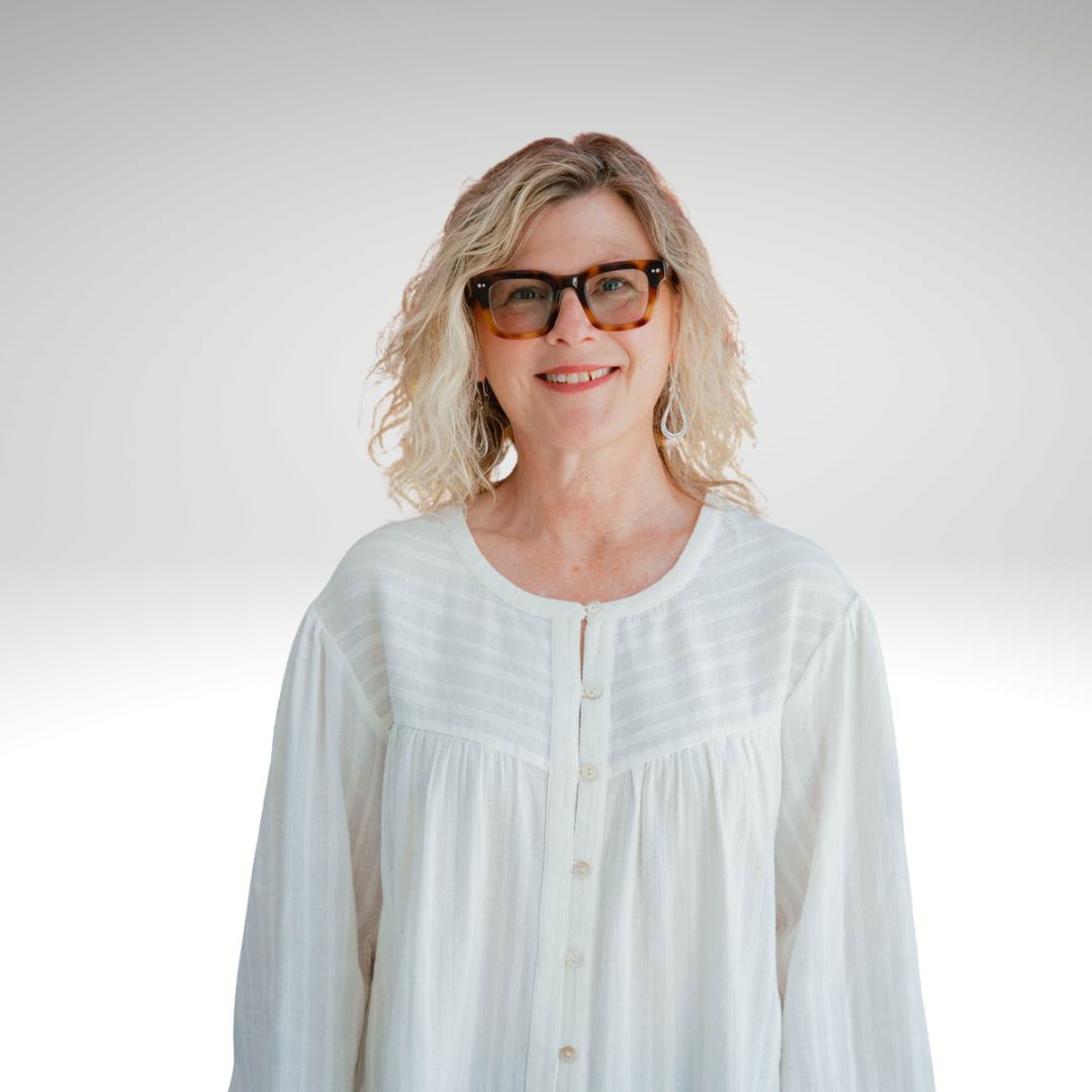 A woman with curly blonde hair wearing glasses with tortoiseshell frames and a white button-up blouse against a plain light background.