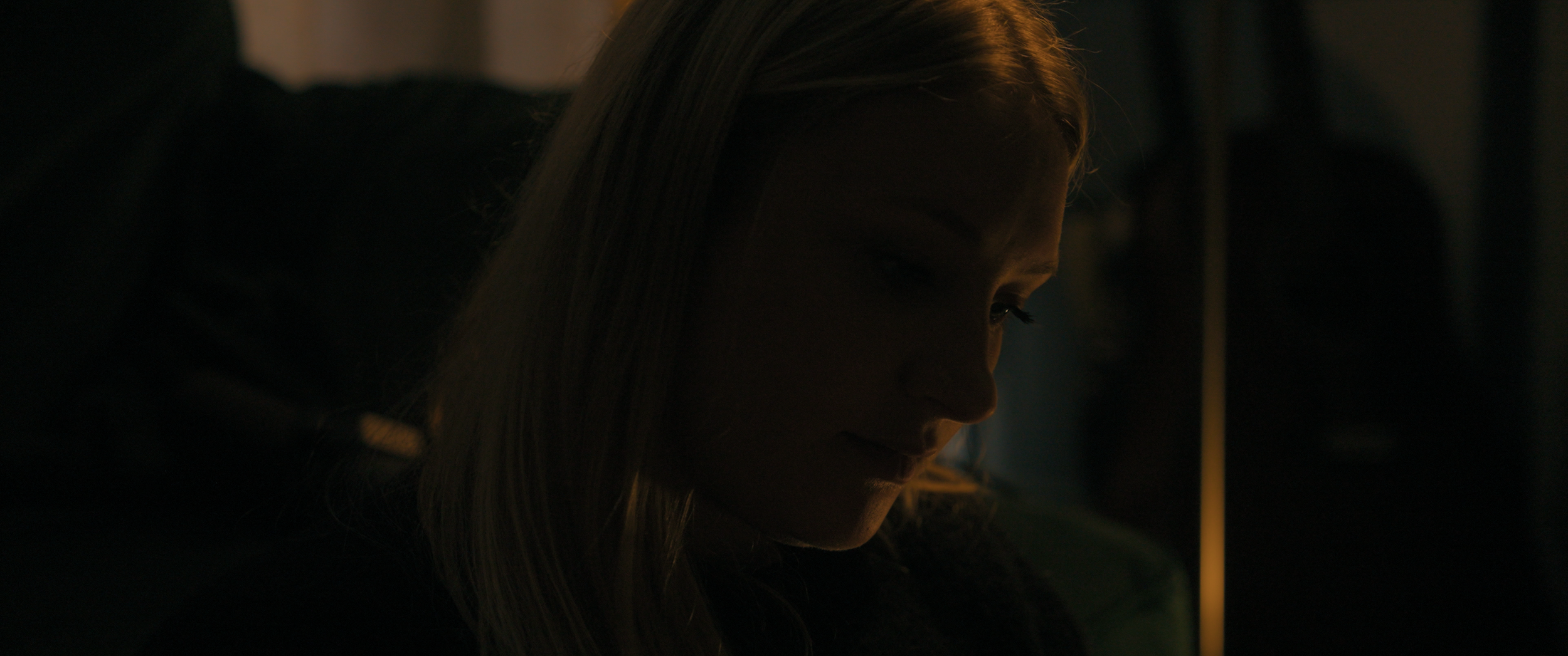 A dark closeup of a woman looking down.