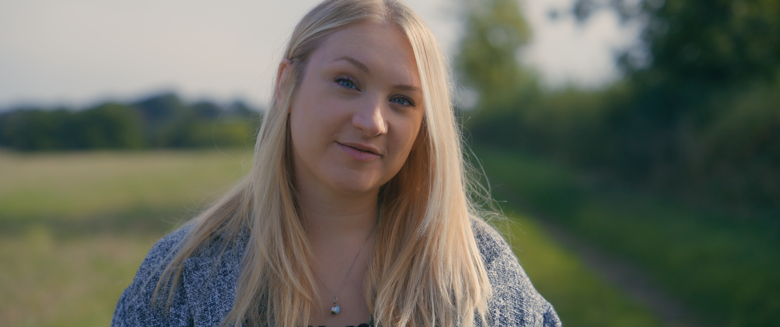 A woman smiles at the camera whilst stood in a field.