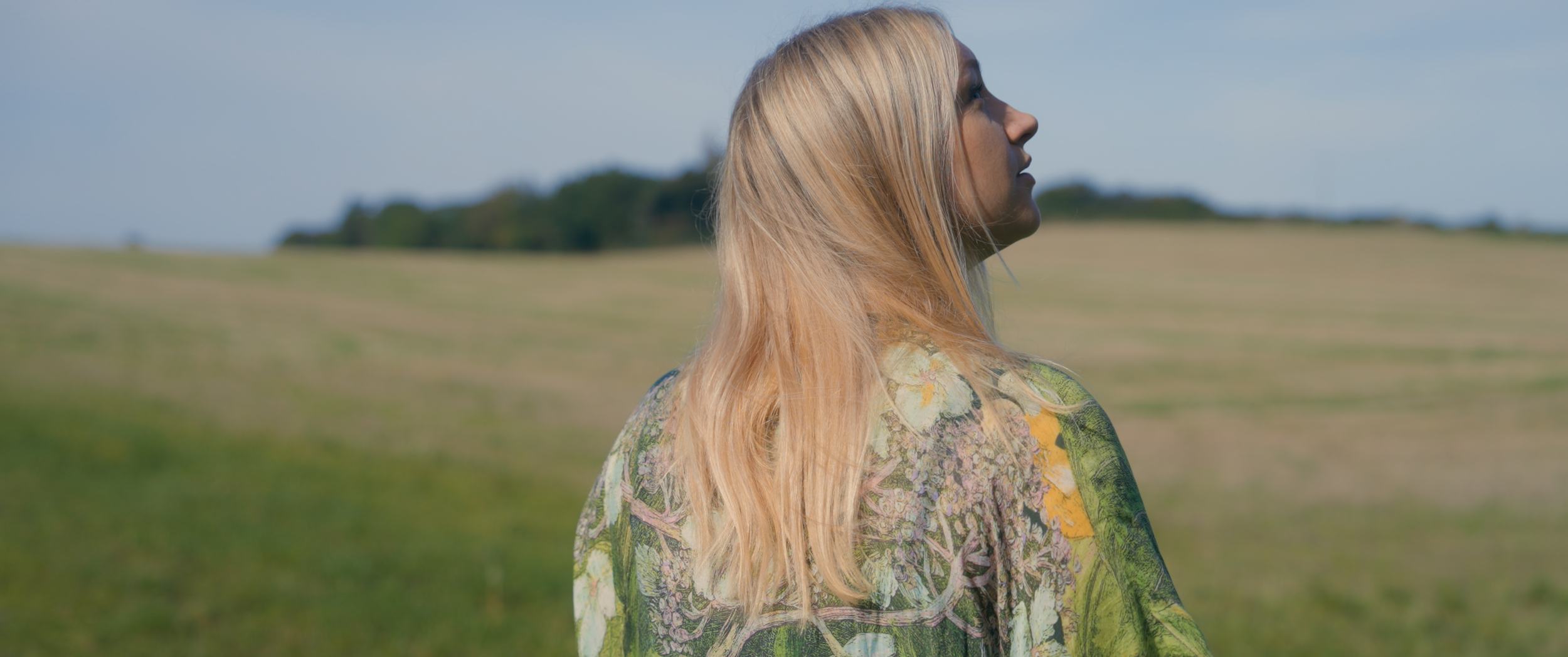A woman stares upwards in front of a field.