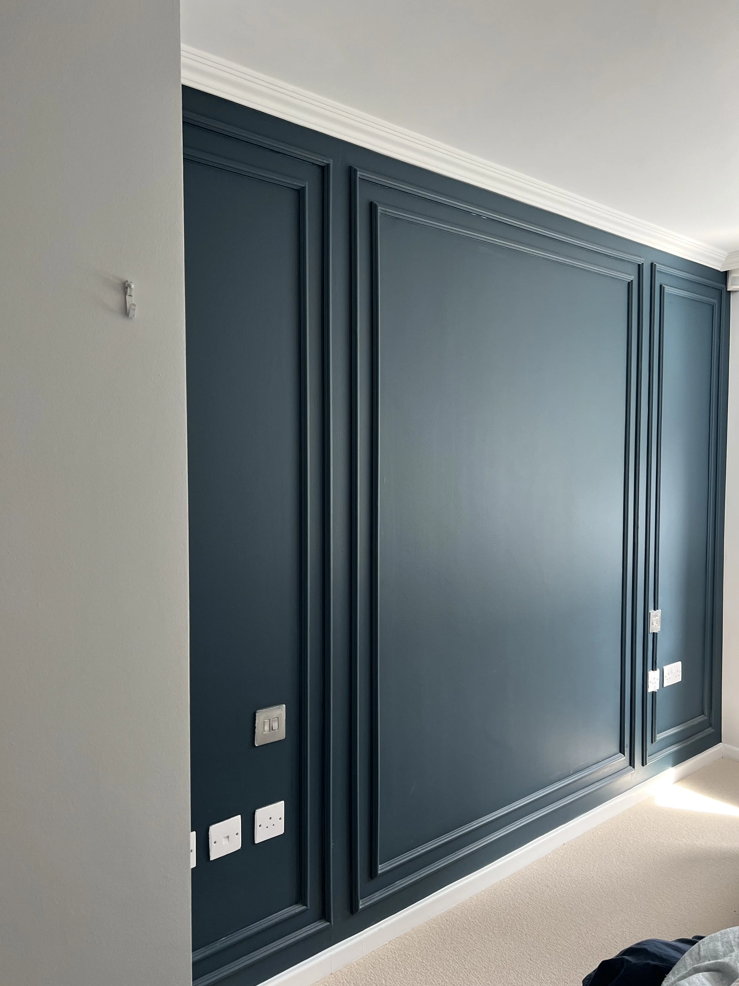 Interior wall with dark teal wainscoting and trim, electrical outlets, and switches.