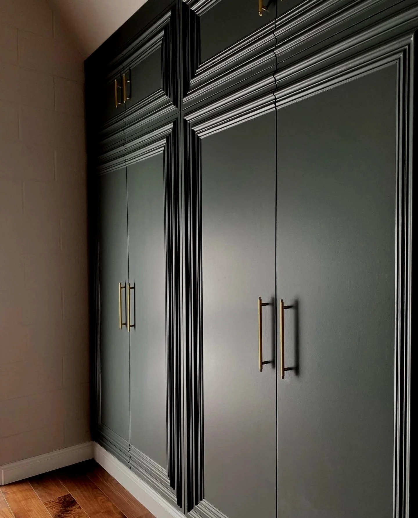 Image of a black cabinet with gold handles against a beige wall and hardwood floor.