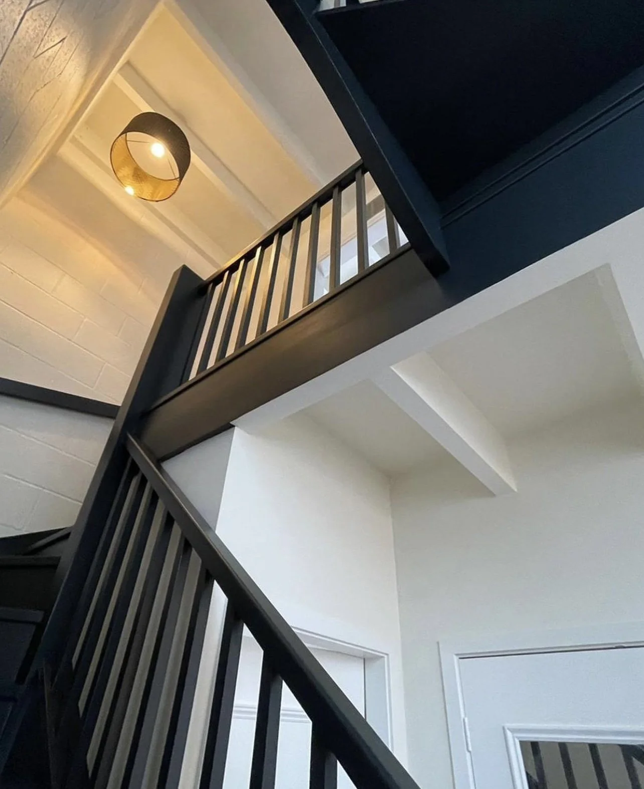 Interior view of a staircase with black railings, white walls, and a ceiling light fixture with a black and gold lampshade.