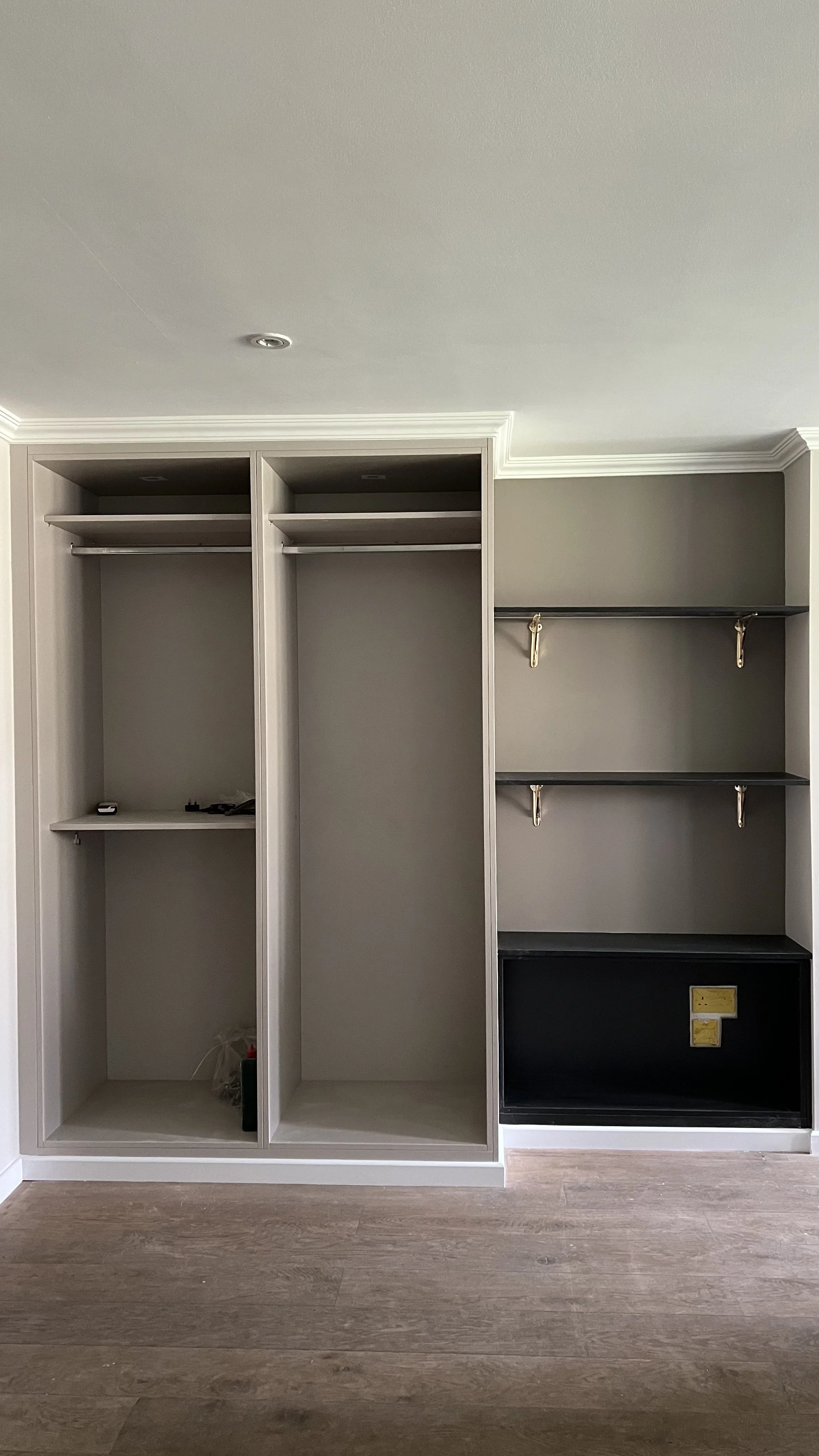 Empty built-in closet with shelves, hanging rods, and a black bottom section in a room with hardwood floors.
