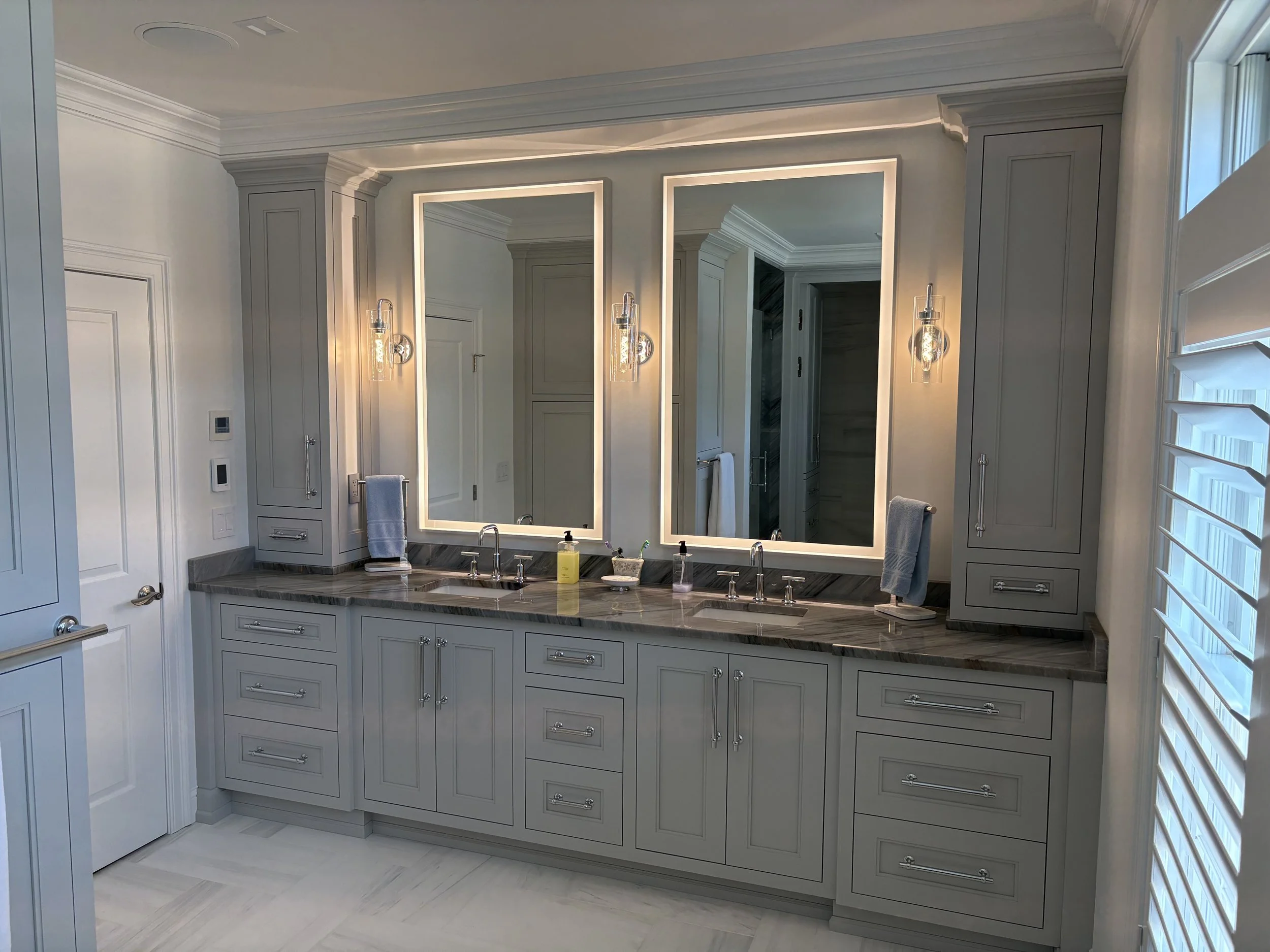 Modern bathroom with double vanity, illuminated mirrors, gray cabinetry, and light fixtures.