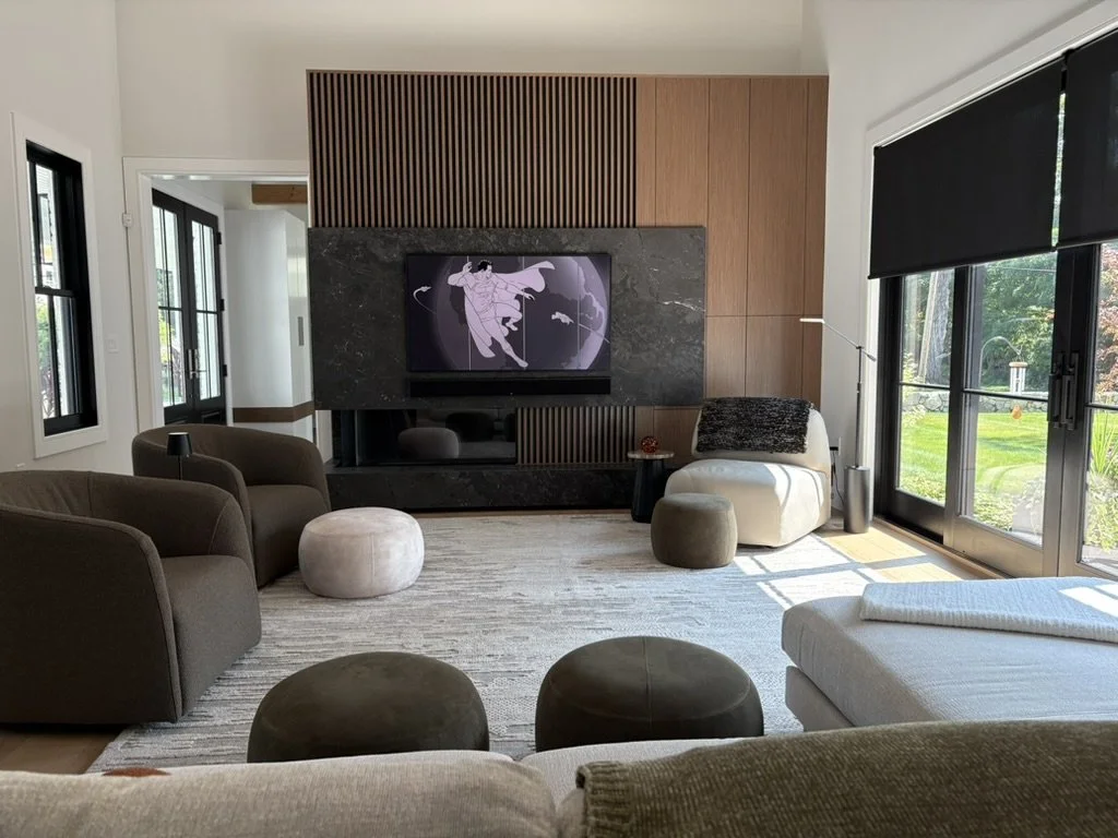 Modern living room with a flat-screen TV displaying a cartoon, dark brown and gray furniture, a large window with black blinds, and natural light.