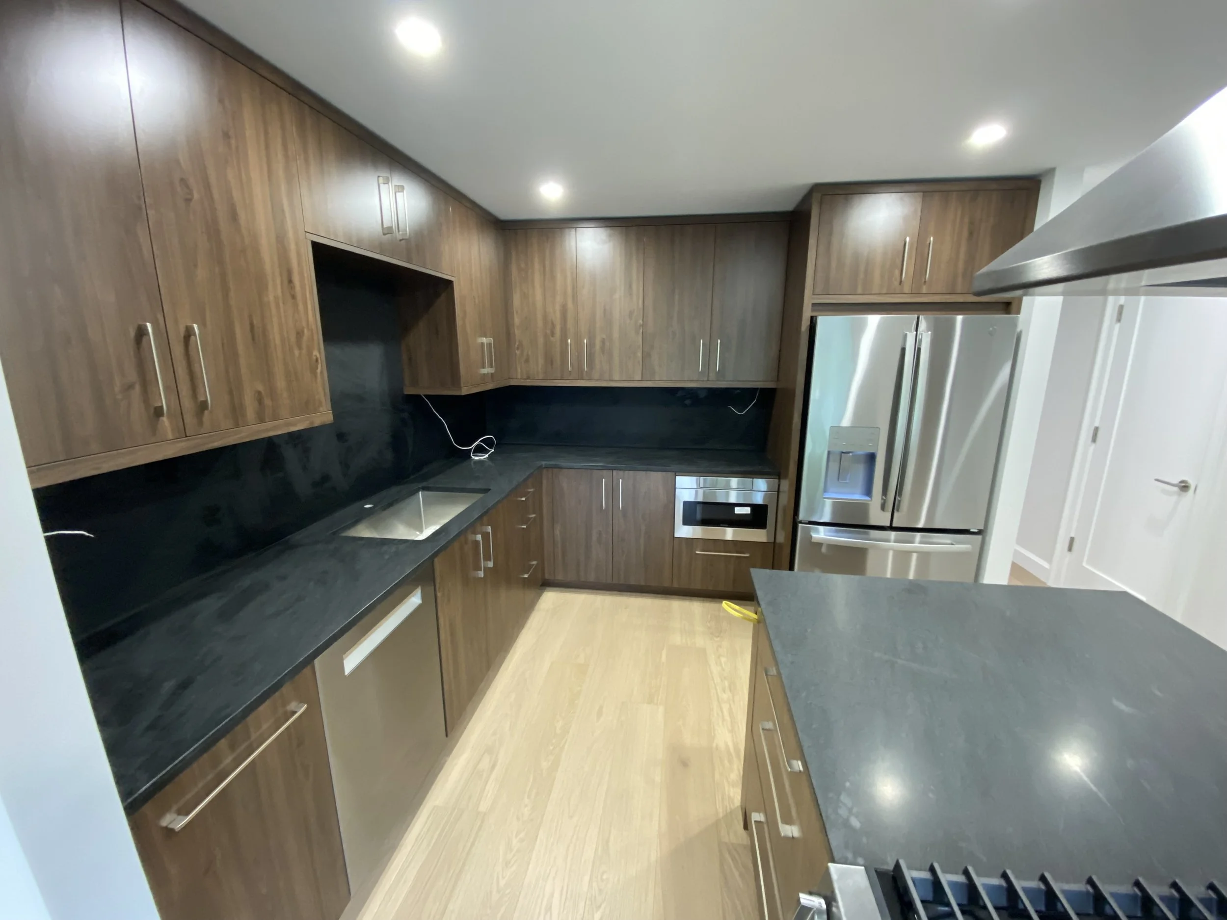 Modern kitchen with wooden cabinets, black countertops, stainless steel refrigerator, oven, and microwave, and a single-basin sink.