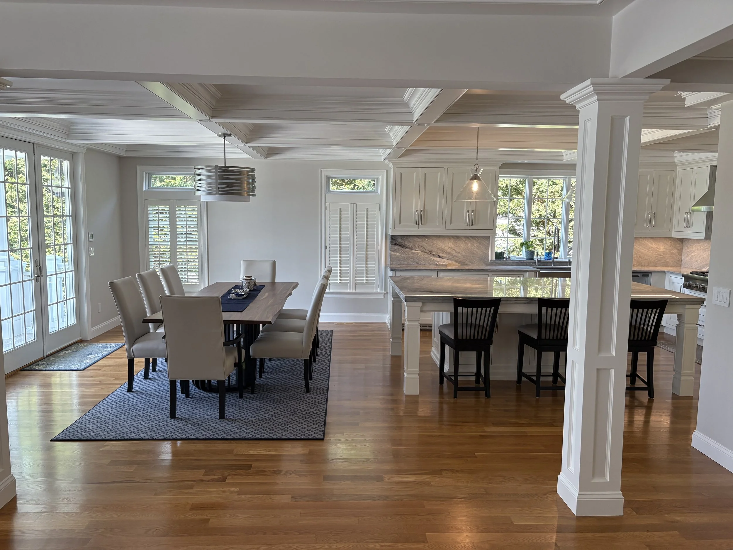 Bright, modern dining and kitchen area with hardwood floors, white cabinetry, and large windows.