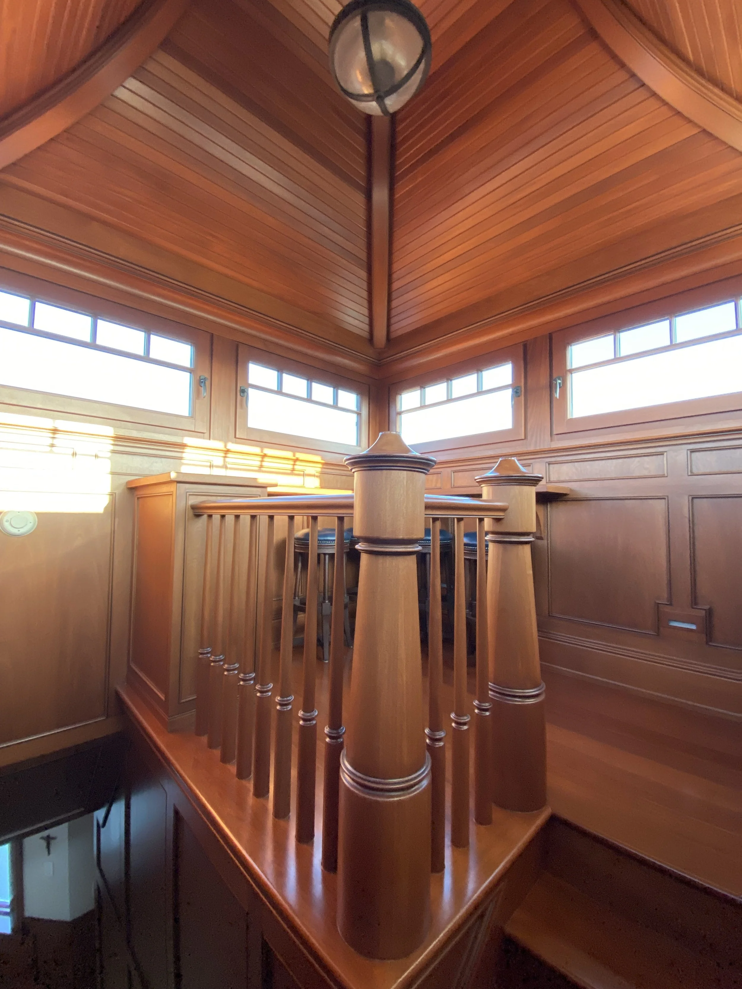 Wood-paneled interior with a corner of windows, wooden railing, and ceiling, with a hanging light fixture.