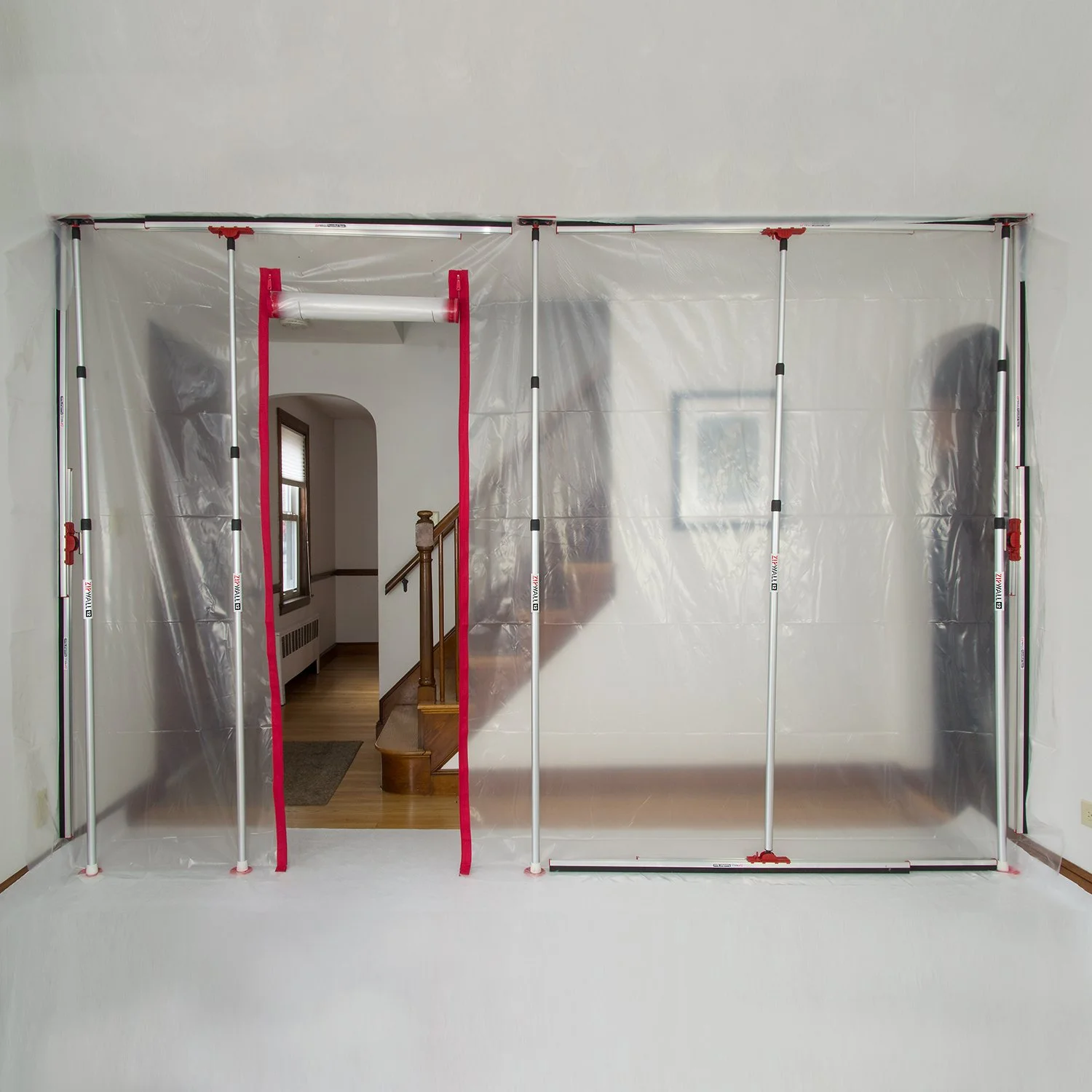 An indoor construction frame with a plastic wall, door opening leading to a staircase and hallway, and a framed picture on the wall.