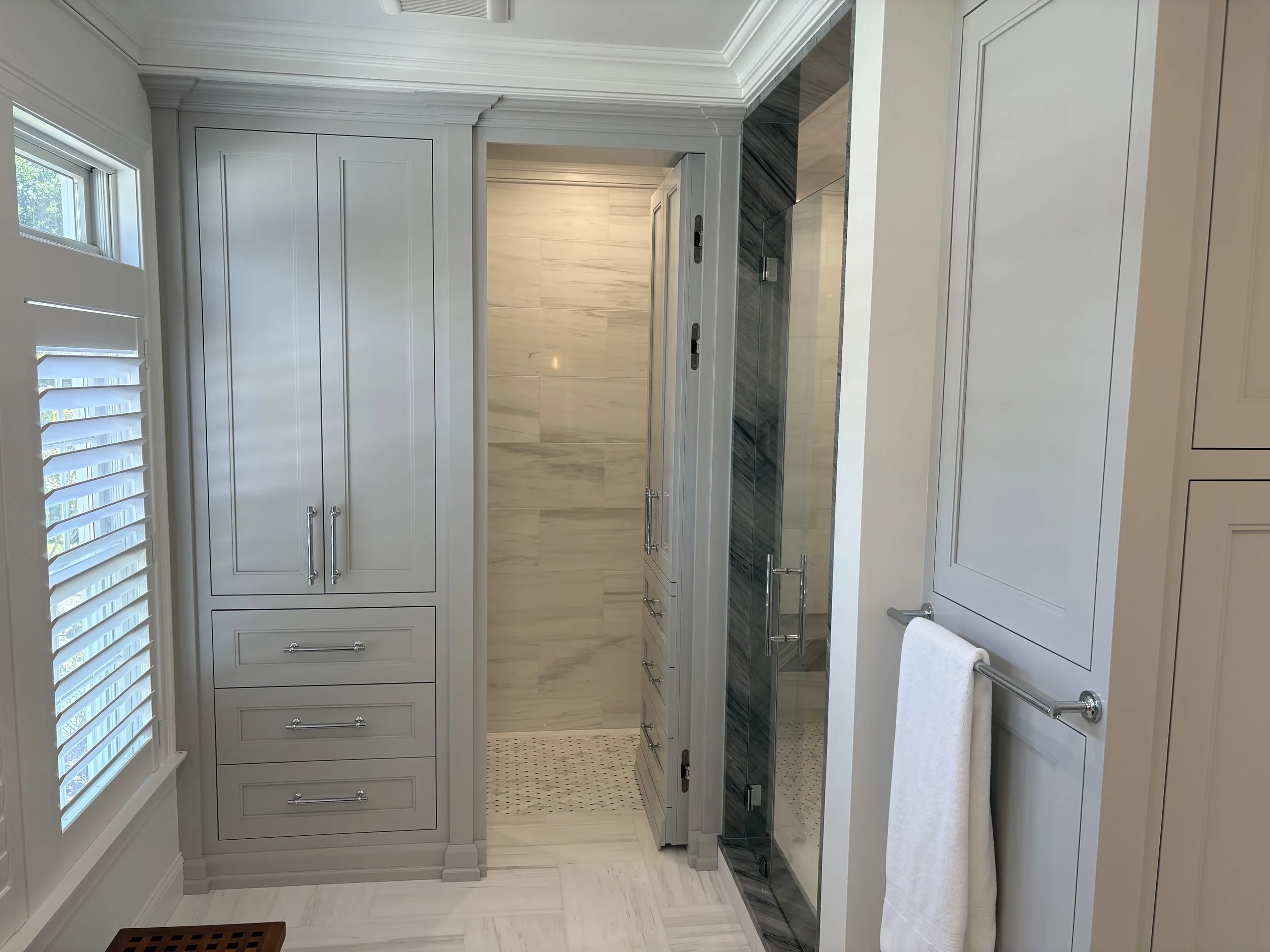 Modern bathroom with white cabinetry, a glass-enclosed shower, and a window with white shutters.