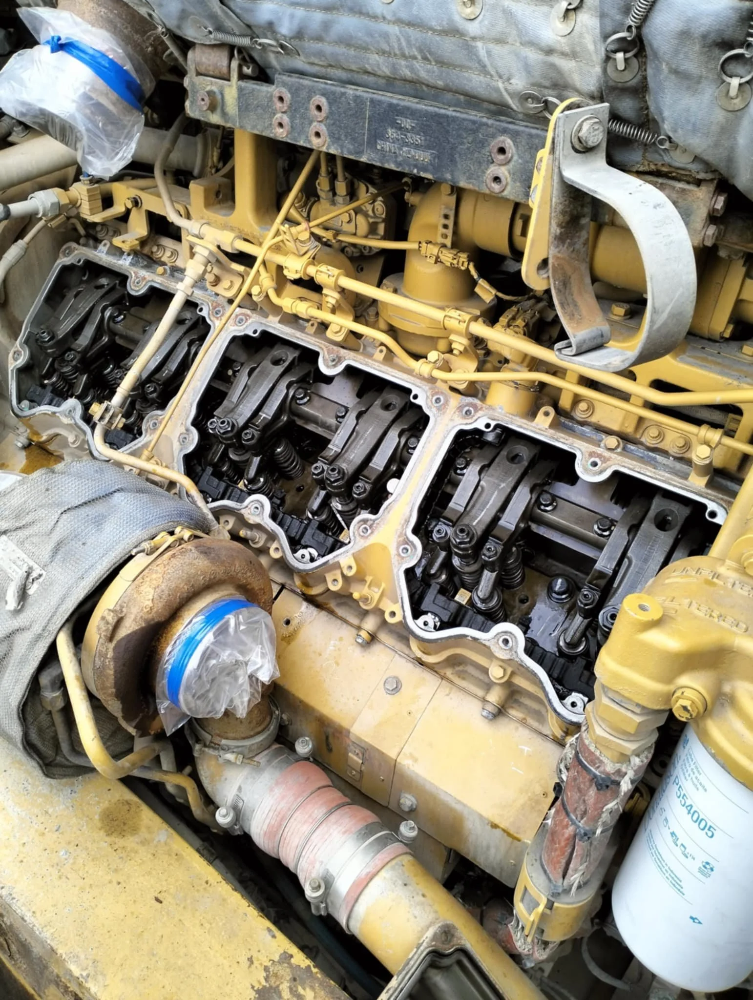 mobile diesel fitter in Toowoomba - CGK Earth & Ag - Close-up of an internal engine with head covers removed, showing pistons, valves, and internal components, in a yellow-painted engine block.