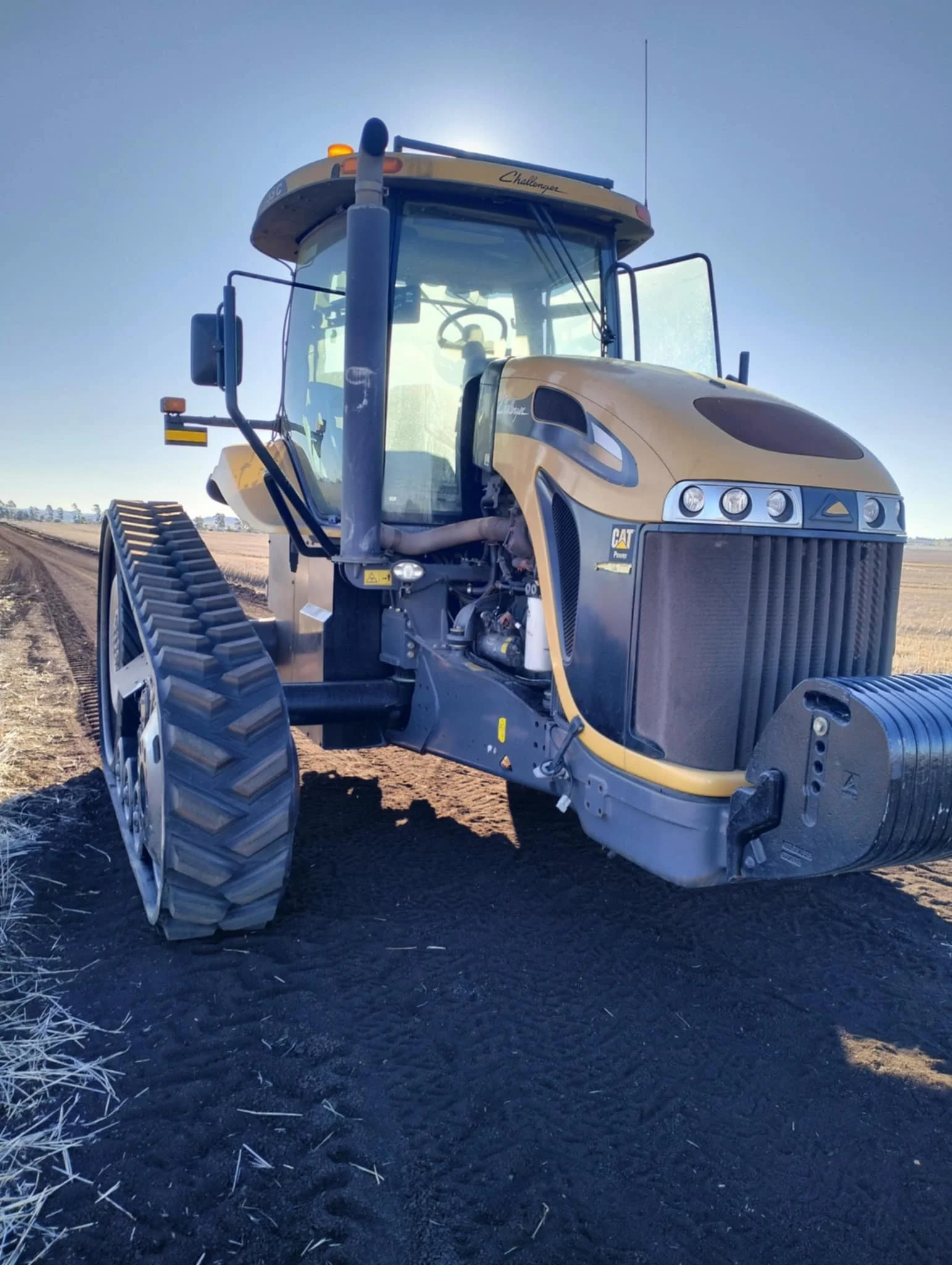 A large yellow and black Caterpillar Challenger tractor on a farm field under a clear sky.