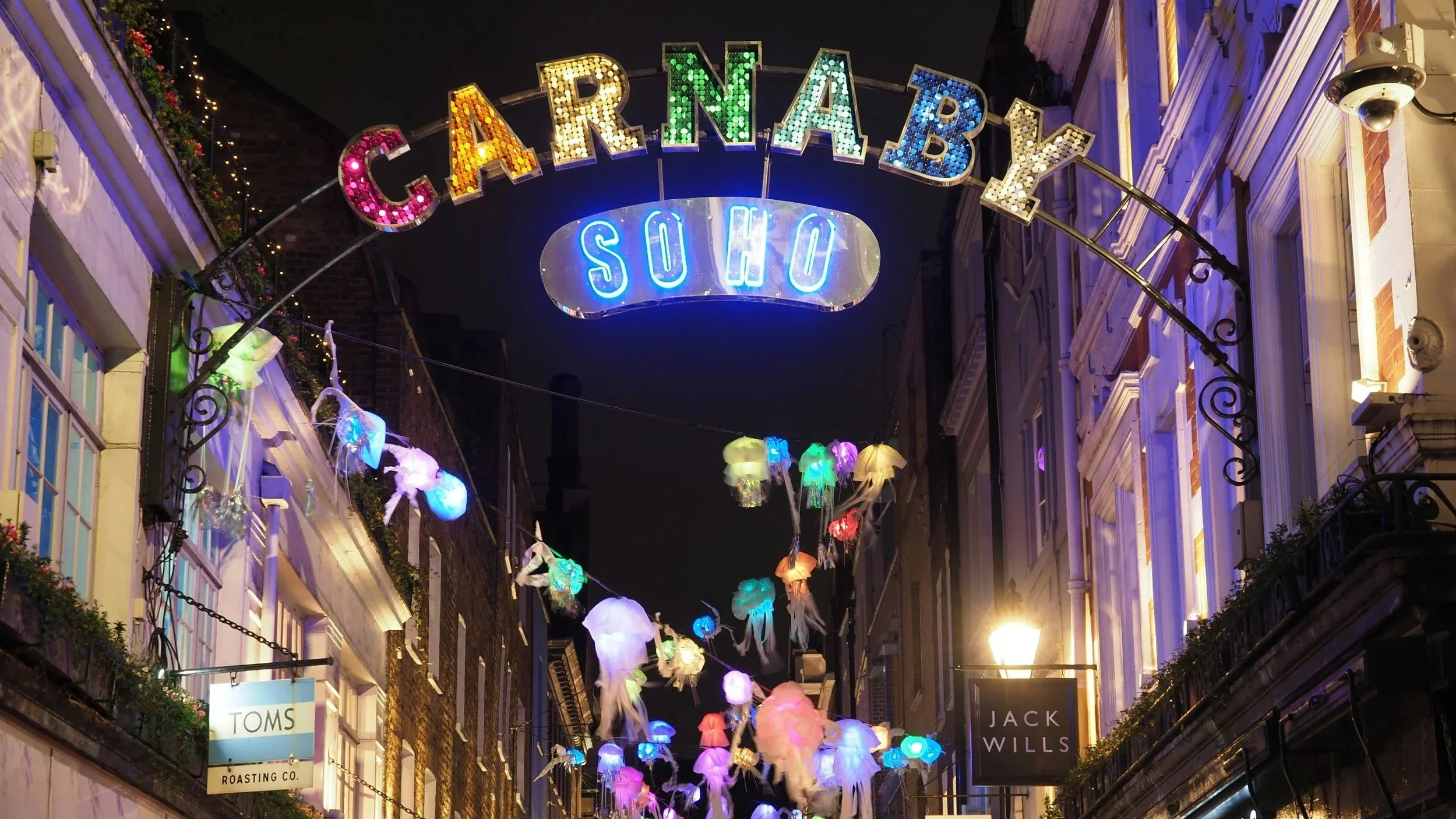 Carnaby Street in Soho London at night time with shop front signs and the famous Carnaby sign.