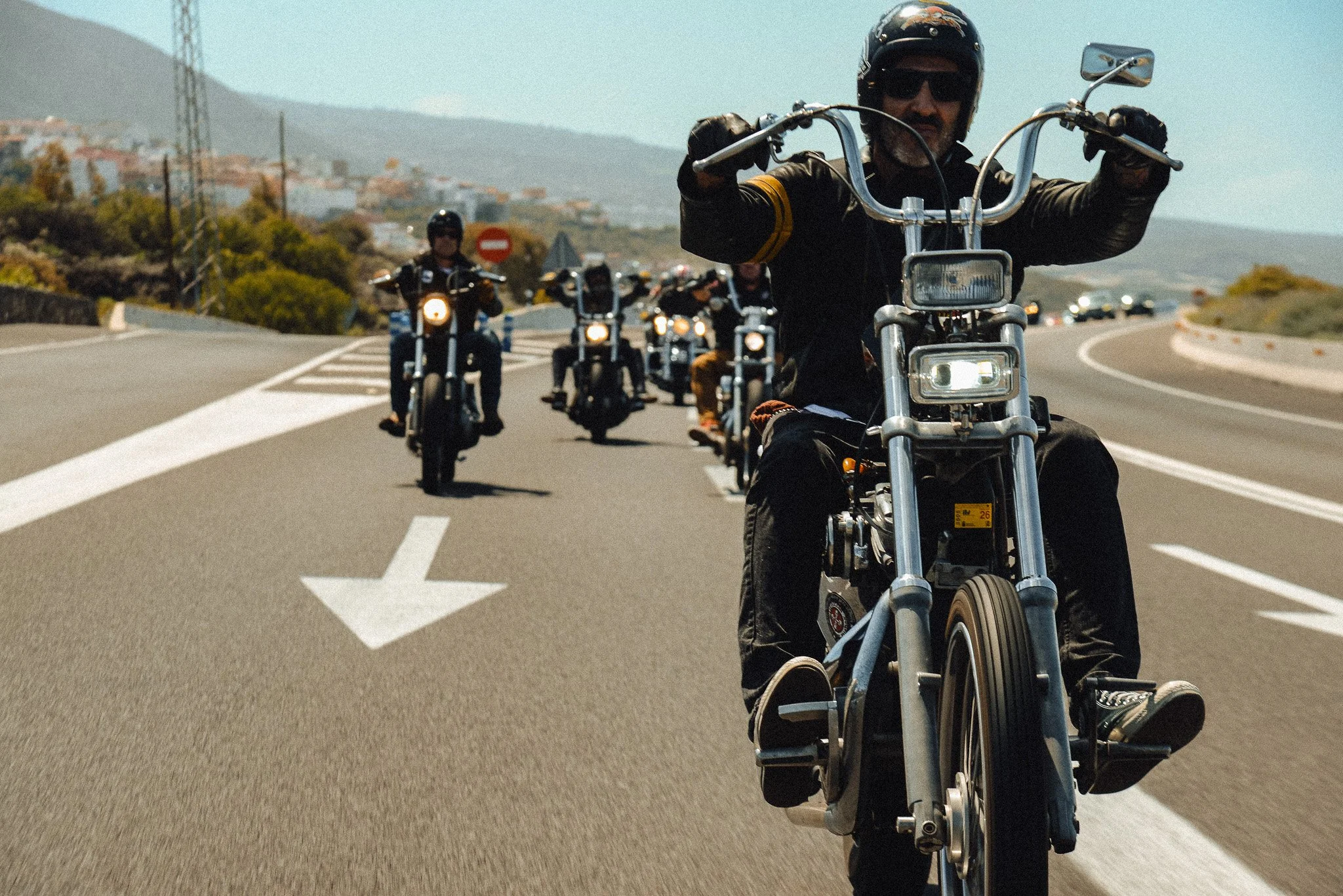 A group of motorcyclists riding in a formation on a highway with a scenic landscape in the background.