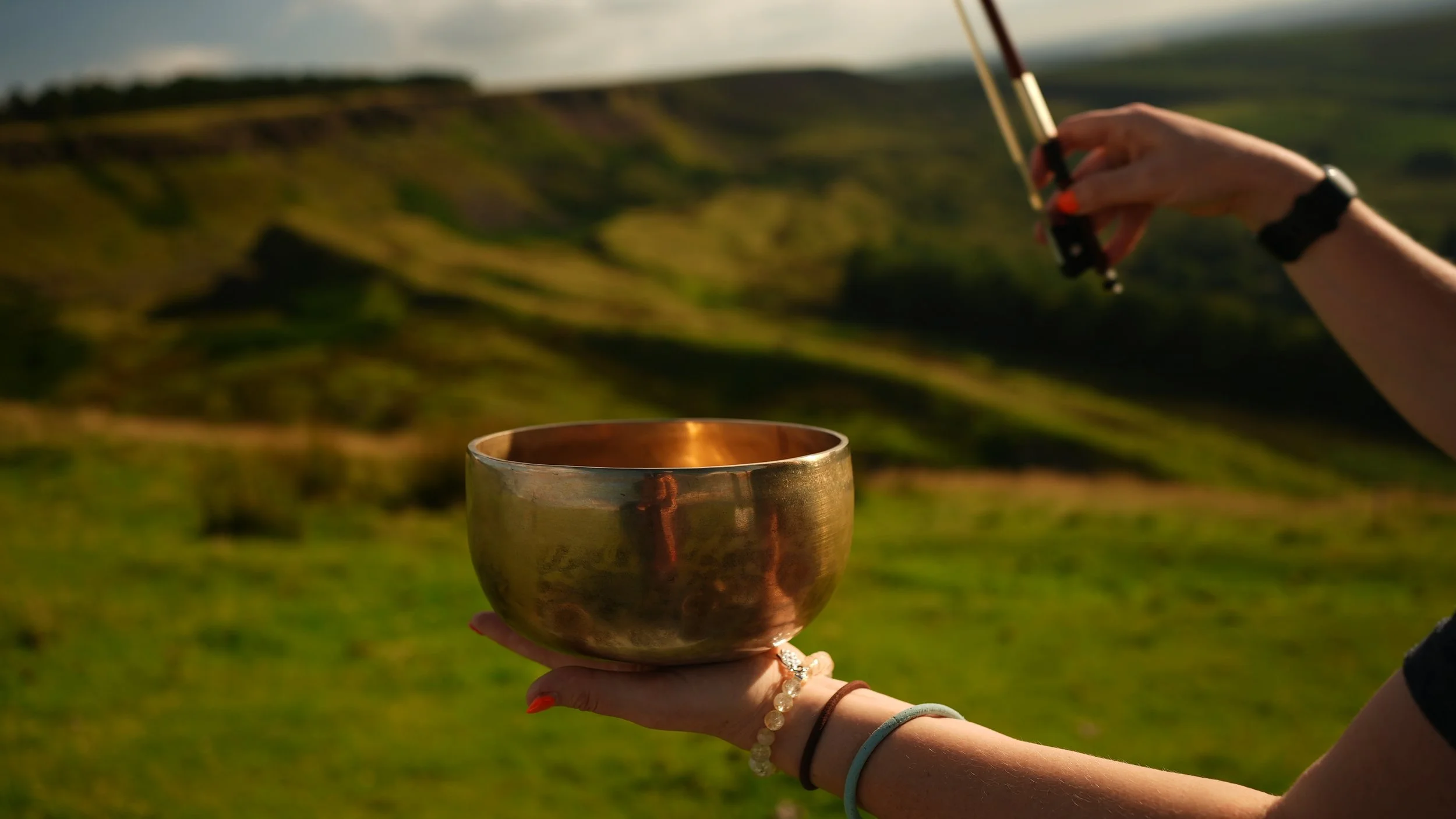 A himalayan singing bowl is held in Clare's left palm, her right hand holds a violin bow about to start playing the bowl any moment