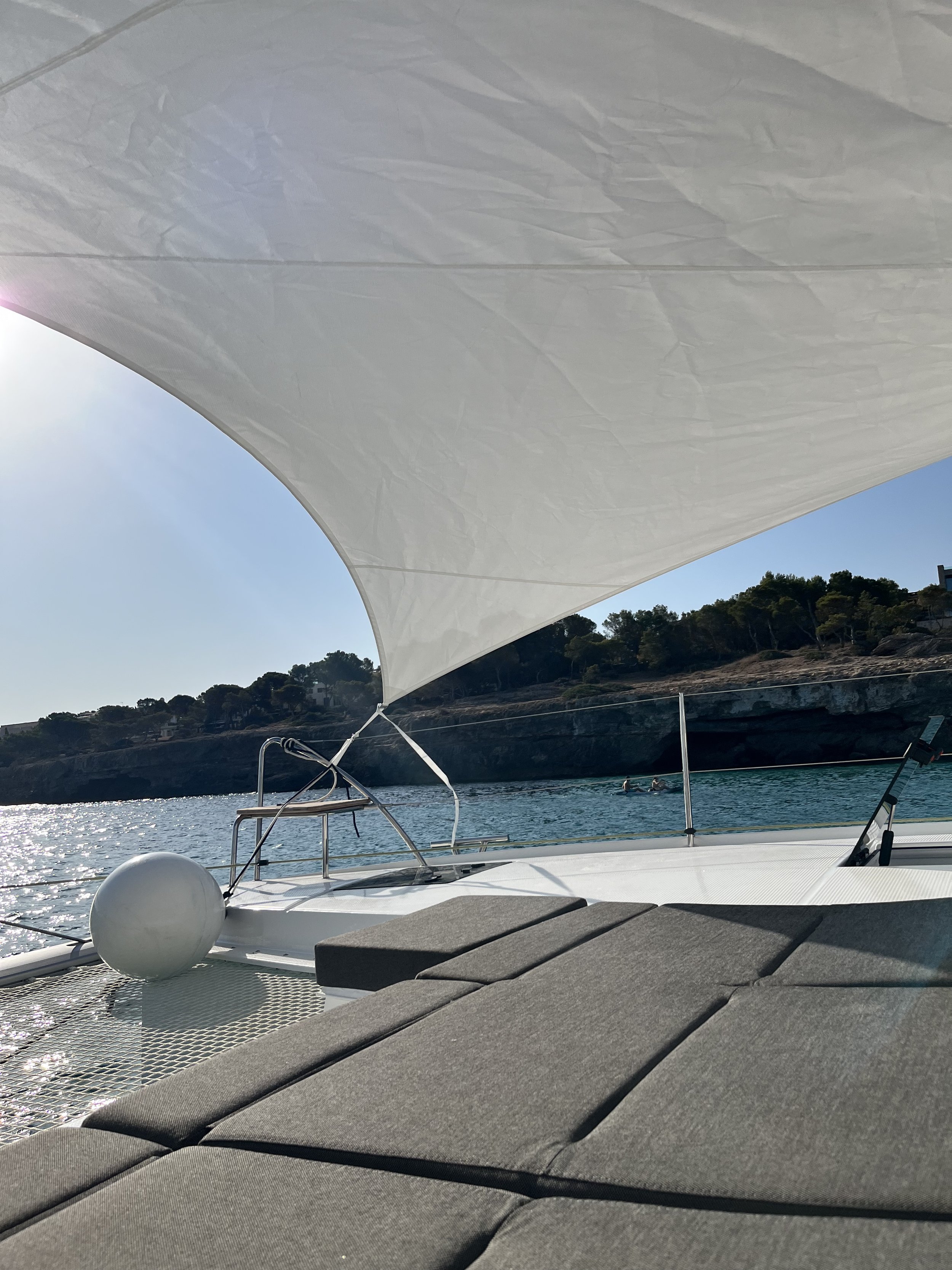 View from a boat with gray cushions, a large white sunshade, and a view of the water with a rocky shoreline and trees in the background.