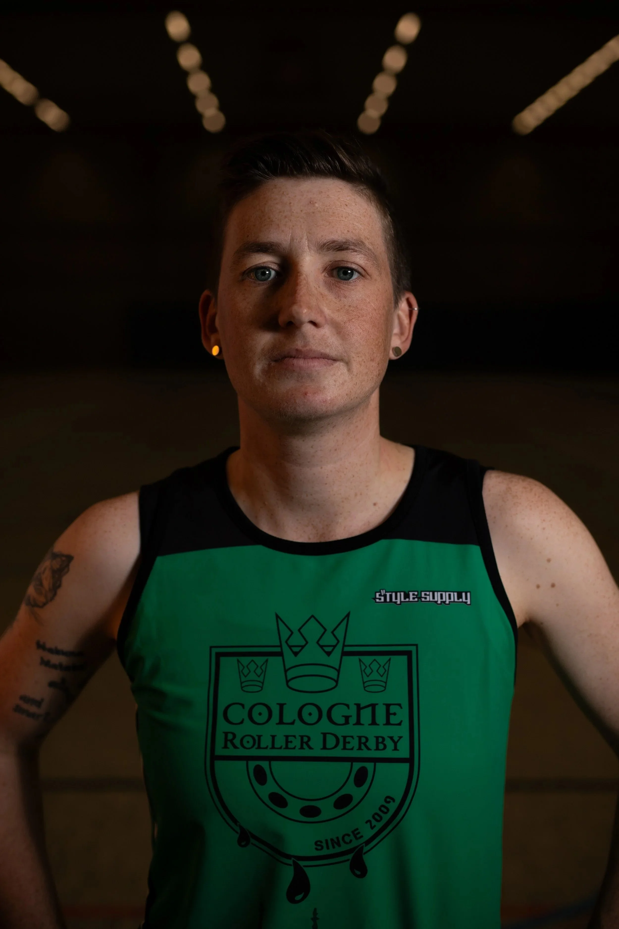 Junge Mann trägt grünes T-Shirt mit Logo und steht in einer Roller Derby Halle.