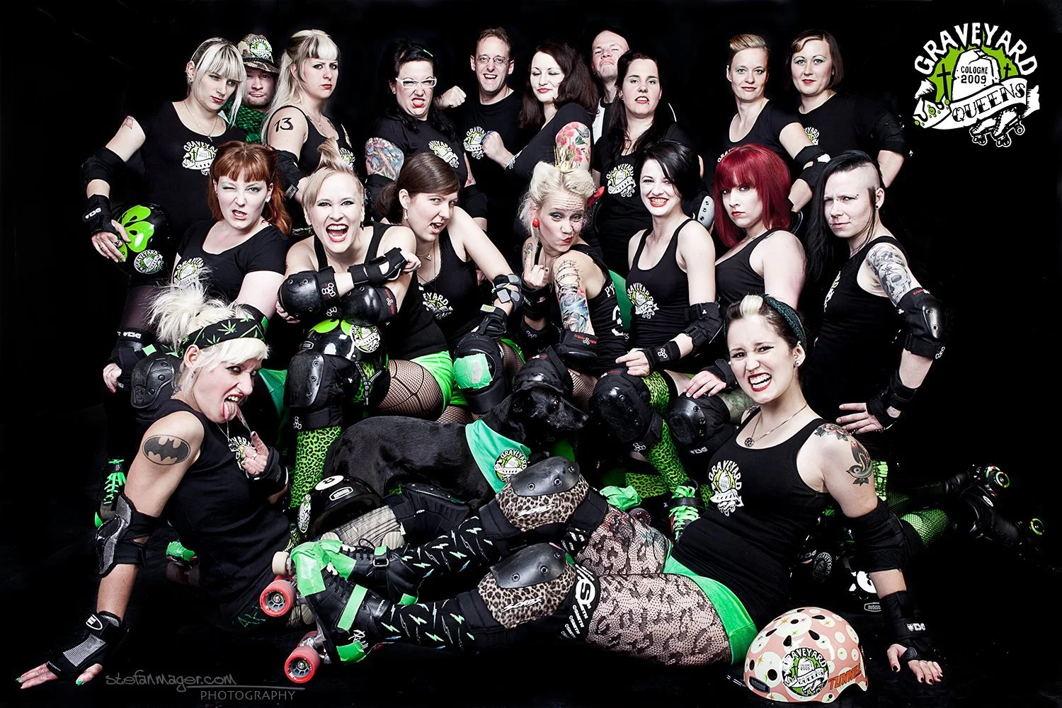 Gruppe von Frauen in Rollschuhen, die in einem Fotostudio mit schwarzem Hintergrund posieren, tragen schwarze Shirts mit einem 2009-Graveyard-Design und auffälligem Make-up; einige haben Tattoos, bunte Haare und tragen Sicherheitsausrüstung wie Knieschützer und Helme.