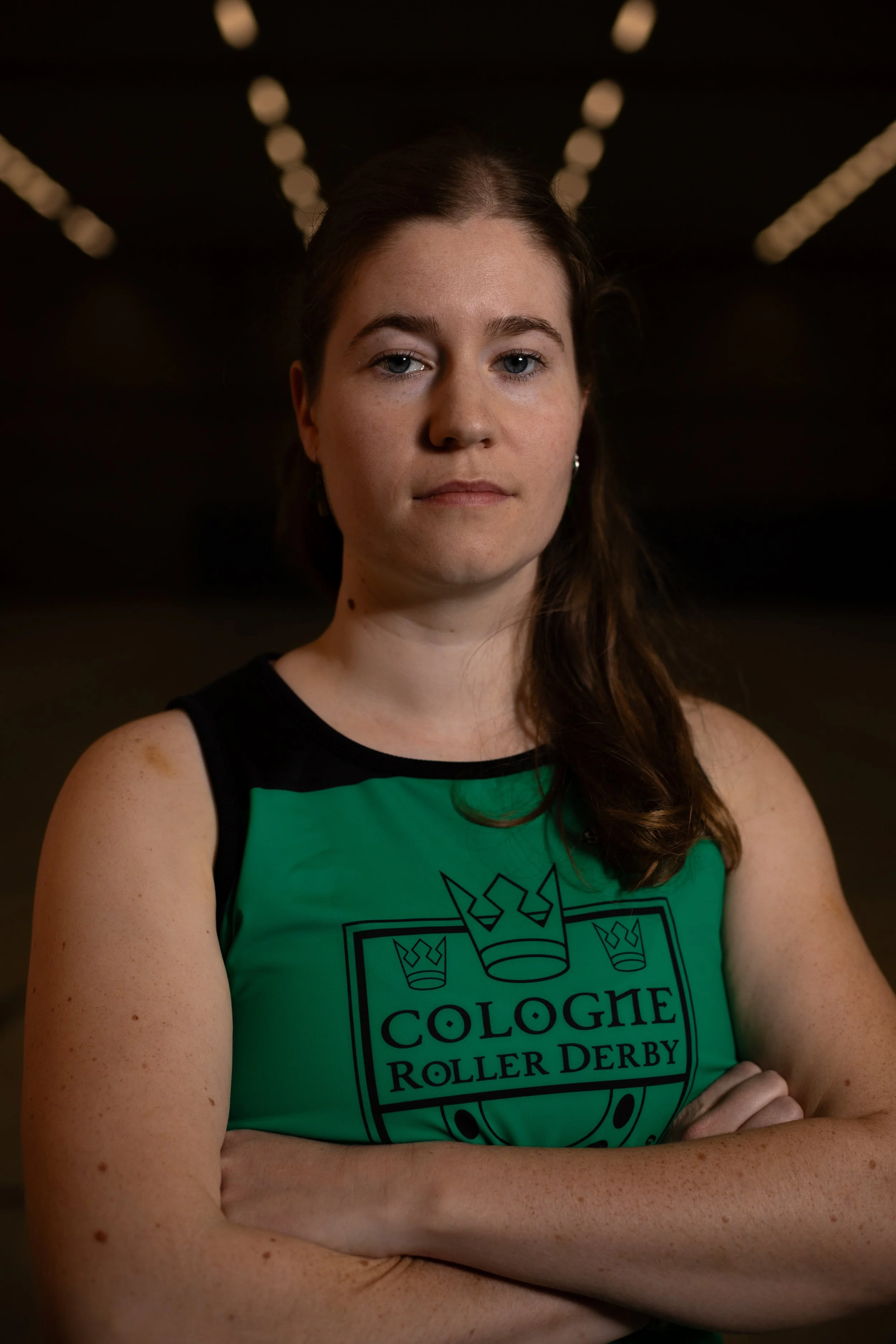 Junge Frau trägt ein grünes Trikot mit der Aufschrift "Cologne Roller Derby" und crossing arms.