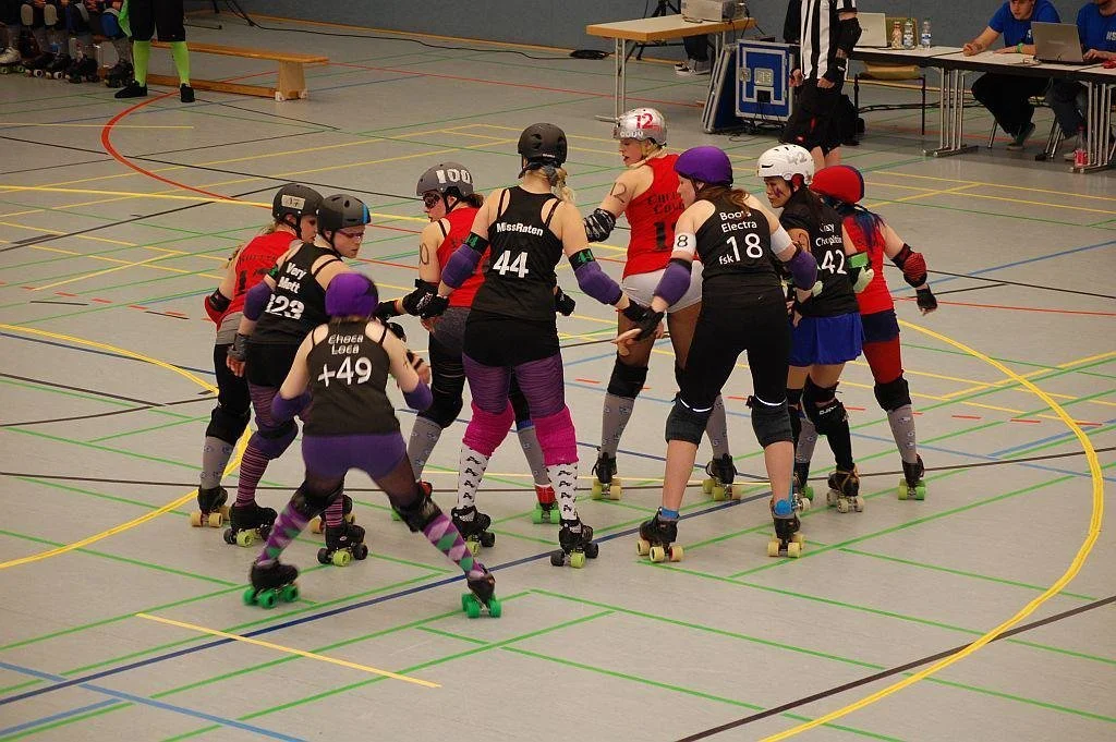 Roller Derby Spielerinnen bilden einen Kreis auf einer Hallenbahn.