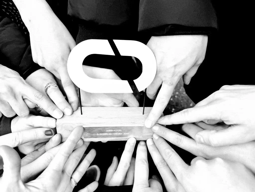 Mehrere Hände, die um einen Preis mit einem großen Buchstaben 'Q' in der Mitte greifen.