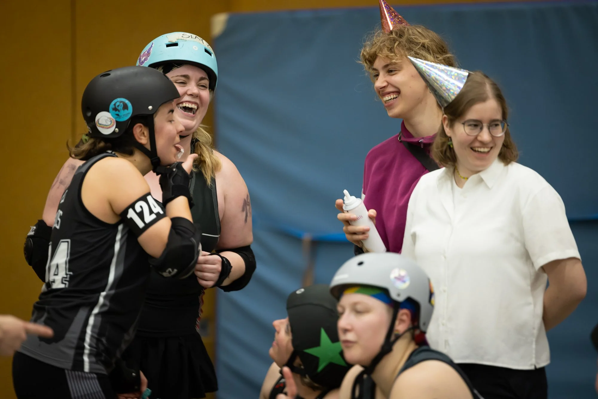 Eine Gruppe von Frauen beim Indoor-Rollhockey, lachend und in Gespräch vertieft. Zwei Frauen tragen Fahrradhelme, während andere einen Party-Hut tragen.