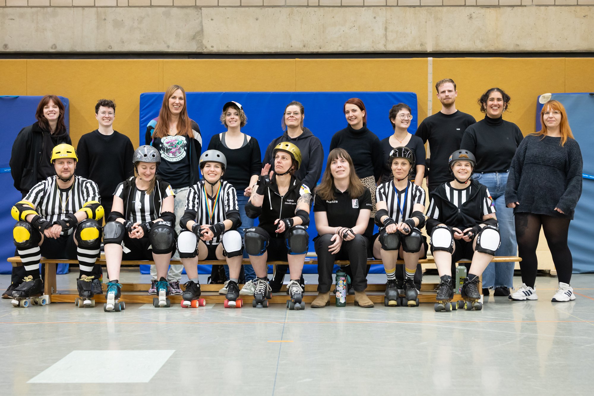 Gruppe von Menschen, einige in Rollschuhen und Schiedsrichter-Kleidung, vor einer Turnhalle.