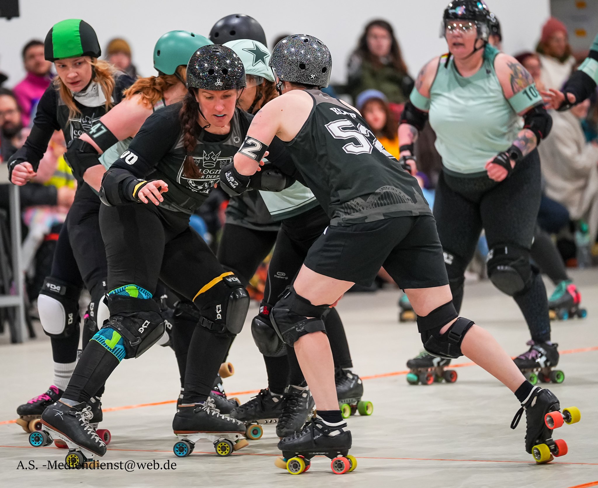 Roller Derby Spielerinnen in einem Kampf auf einer Indoor-Bahn, mit Schutzkleidung und Rollschuhen, die sich im Kampf befinden.