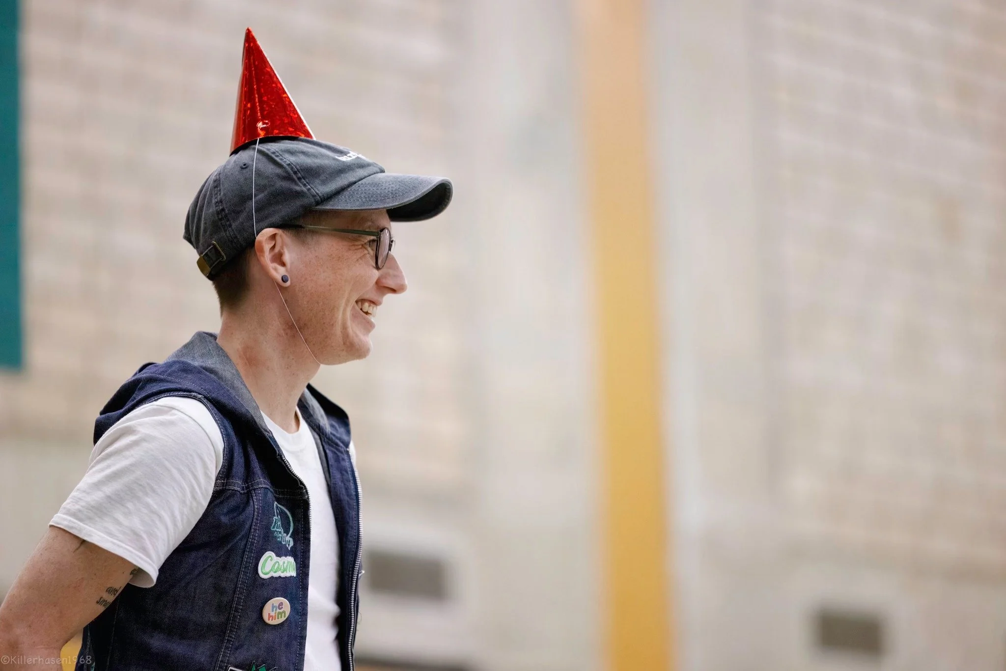 Eine Person trägt einen Partyhut und lächelt, während sie seitlich fotografiert wird.