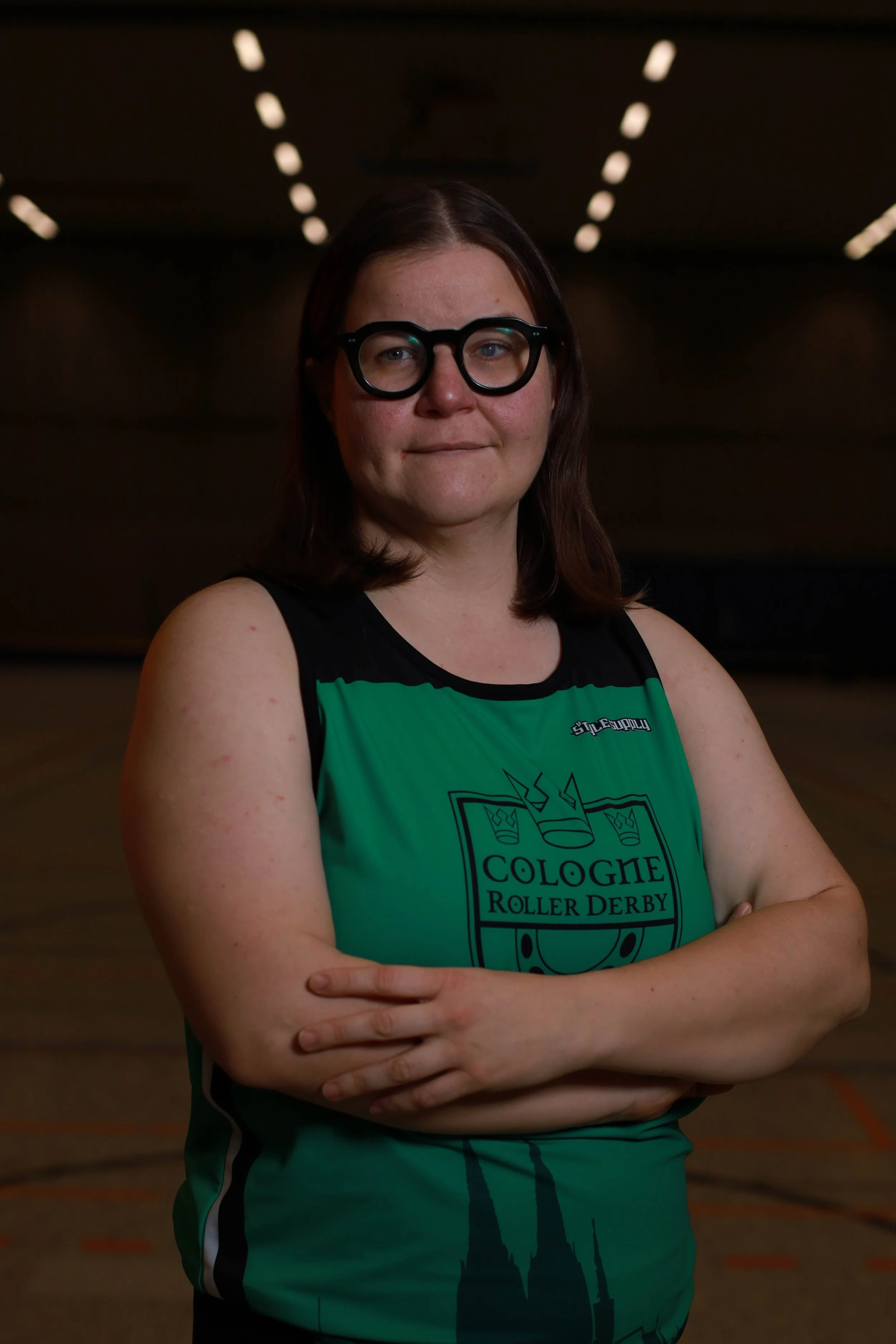 Frau in Rollschuh-Trikot mit Armen verschränkt in einer Rollschuhlaufhalle
