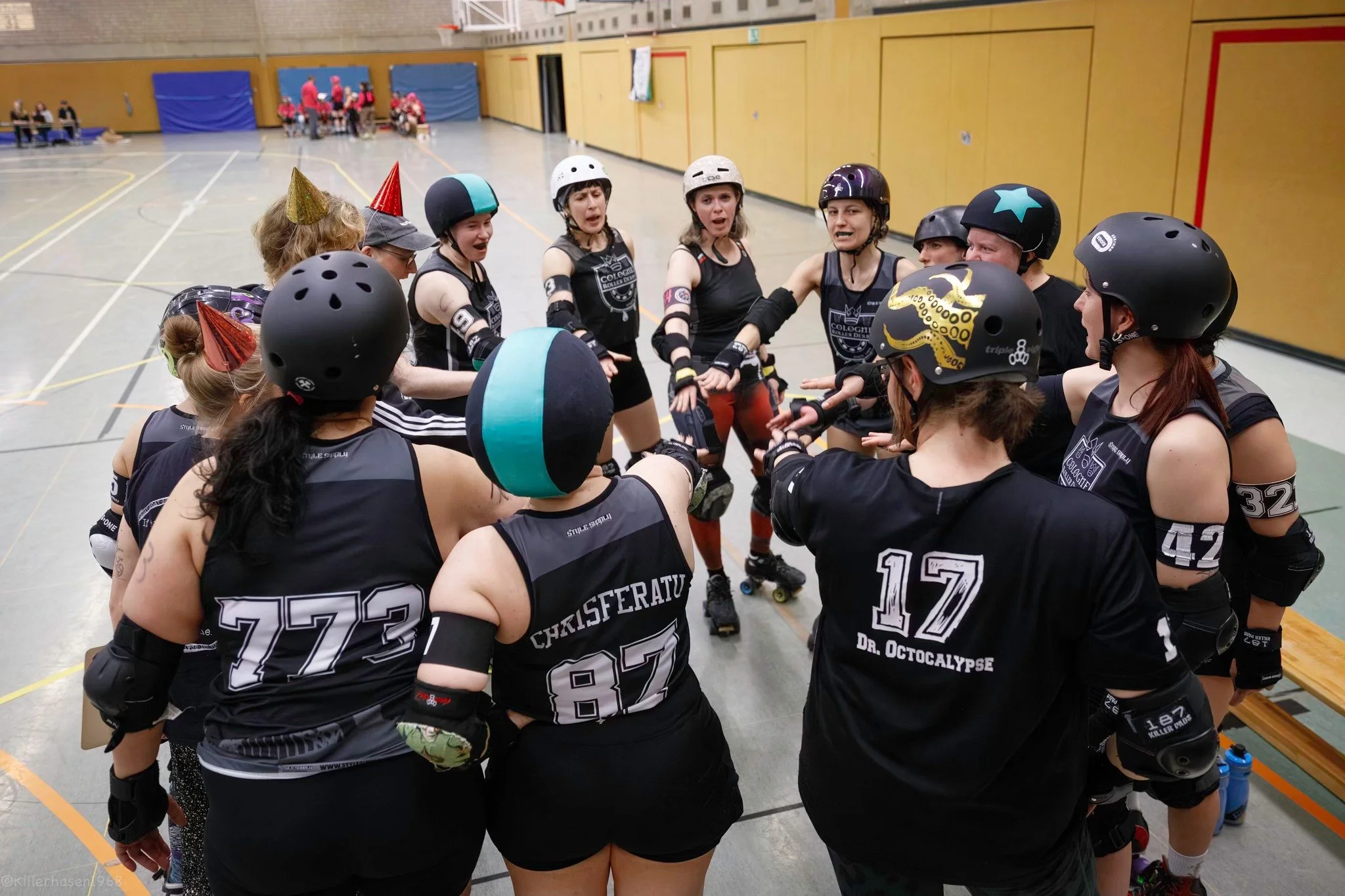 Rollerderby-Team in einer Halle im Kreis, beim Huddle, mit Helmen und Streetwear, die sich vor einem Spiel oder Training motivieren.