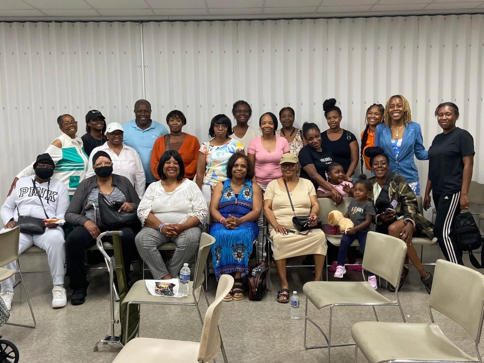 Group of adults, some sitting in chairs and others standing, smiling for a group photo.