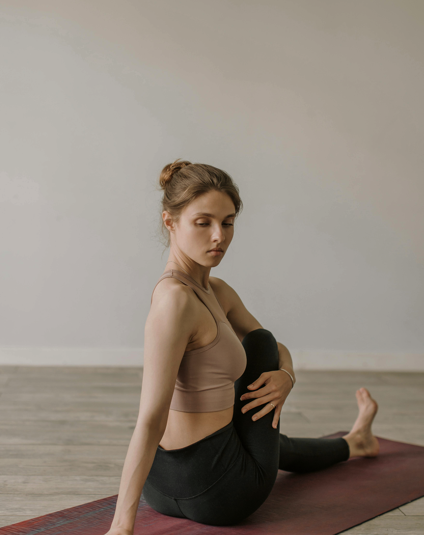 Une femme en tenue de yoga, en position d'étirement sur un tapis de yoga en bois, dans une pièce à murs clairs.
