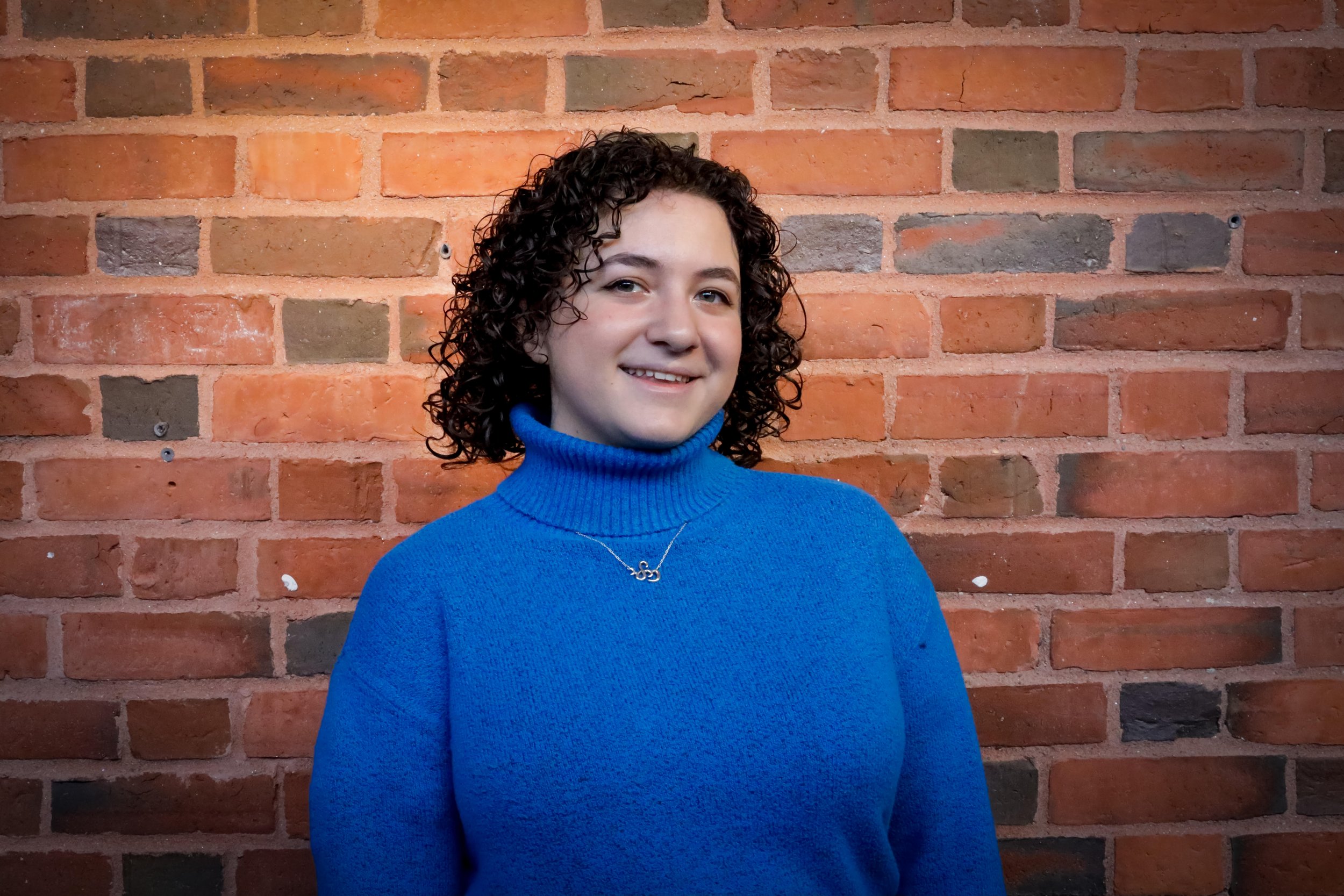 Symbiosis team member smiling outdoors, standing in front of green foliage and plants.